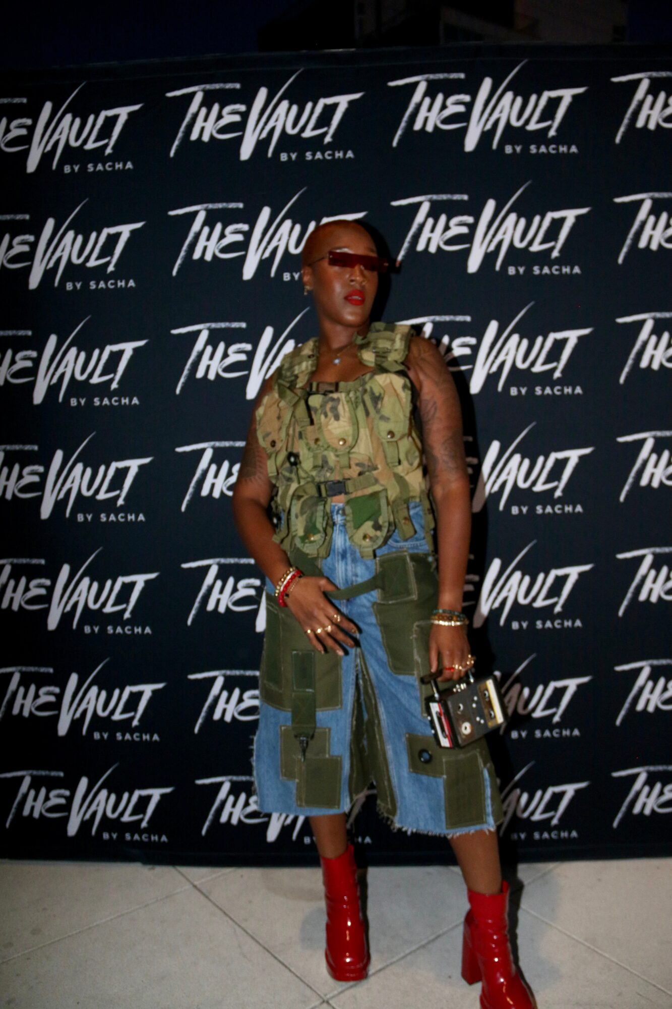 Person standing in front of a black backdrop with white text, wearing a colorful outfit and red boots.
