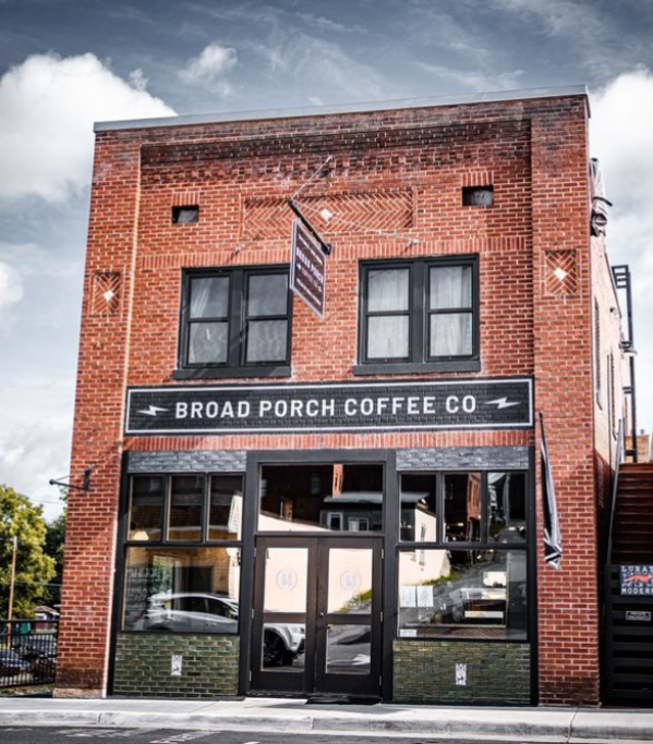 Brick building with a sign for Broad Porch Coffee Co, two windows, and a glass door, under a cloudy sky.