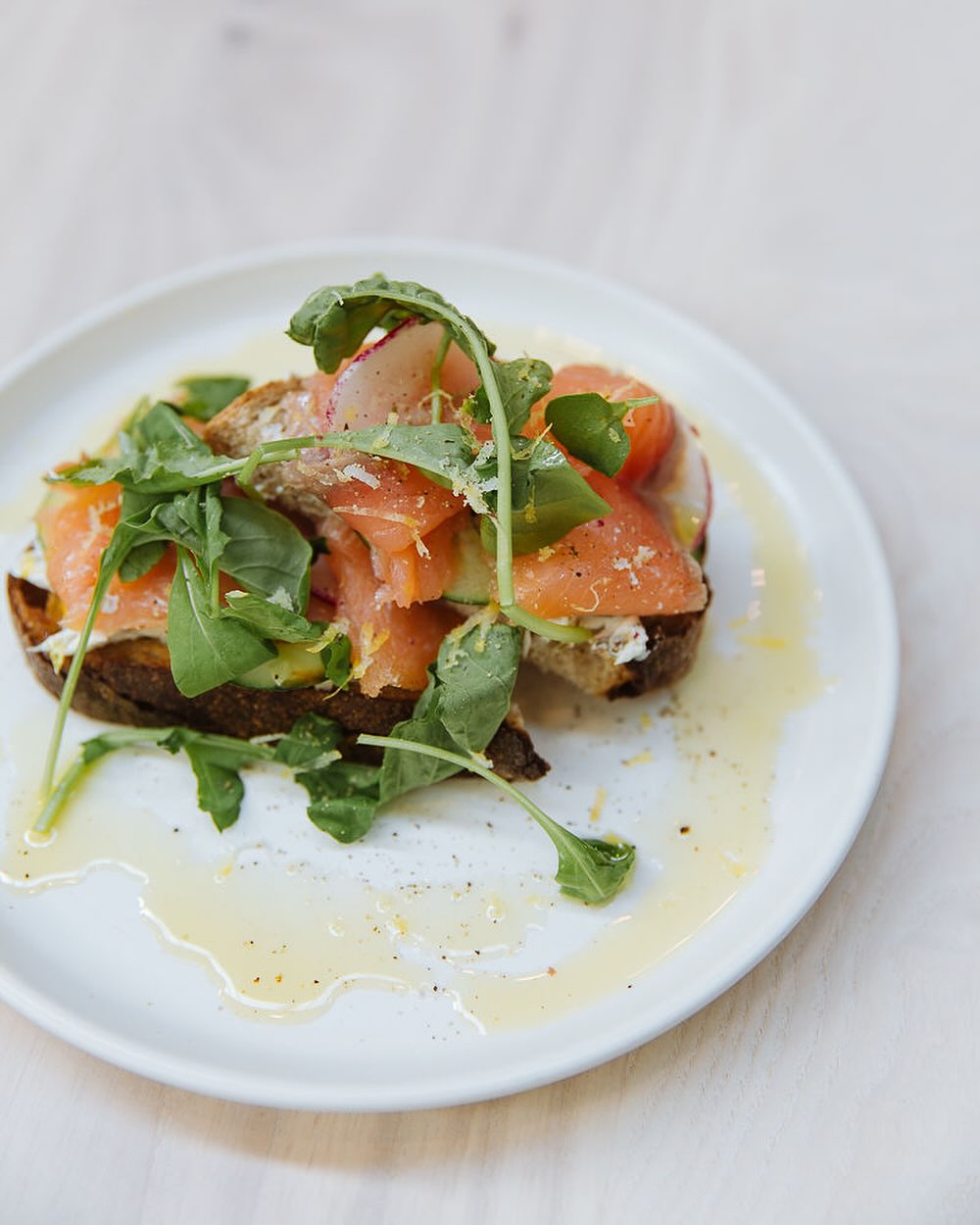 Slices of smoked salmon on bread with arugula and olive oil on a white plate.