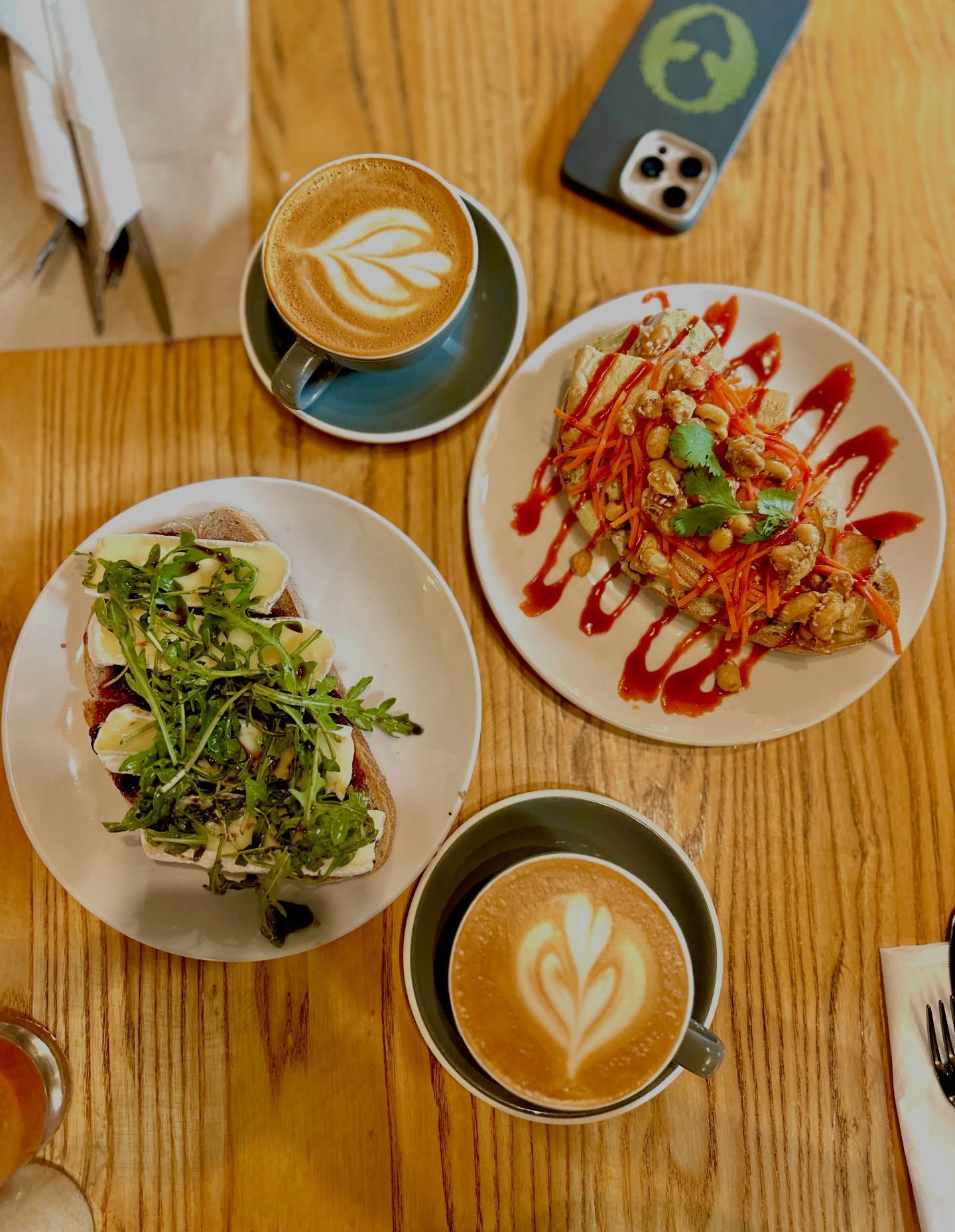 Two cups of coffee with latte art, a plate of salad, and a plate of dessert with strawberries on a wooden table.
