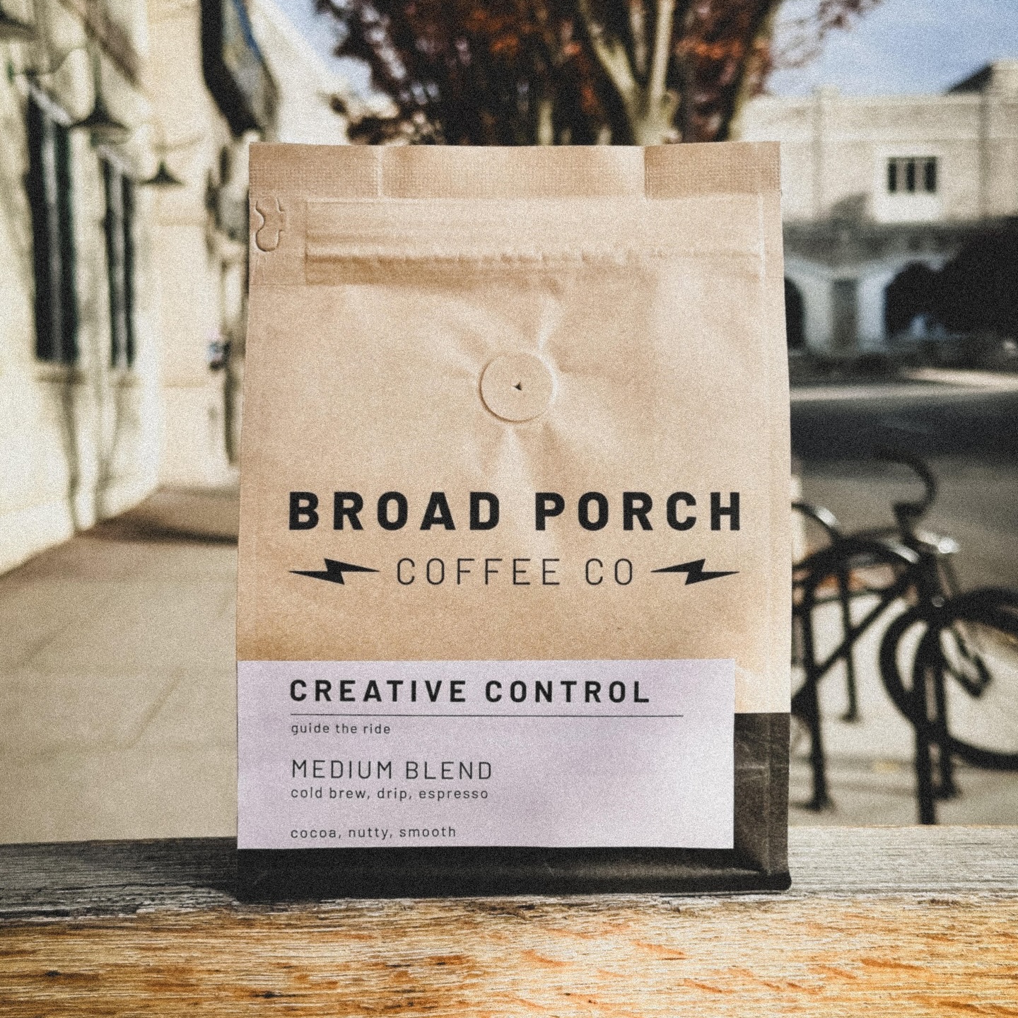 Bag of coffee labeled 'Broad Porch Coffee Co' with 'Creative Control' blend, medium roast, on a wooden surface outdoors.