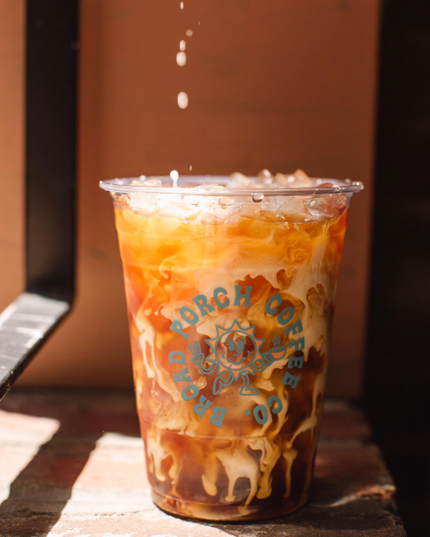 Iced coffee with milk and syrup in a clear cup on a wooden surface, with a logo on the front.