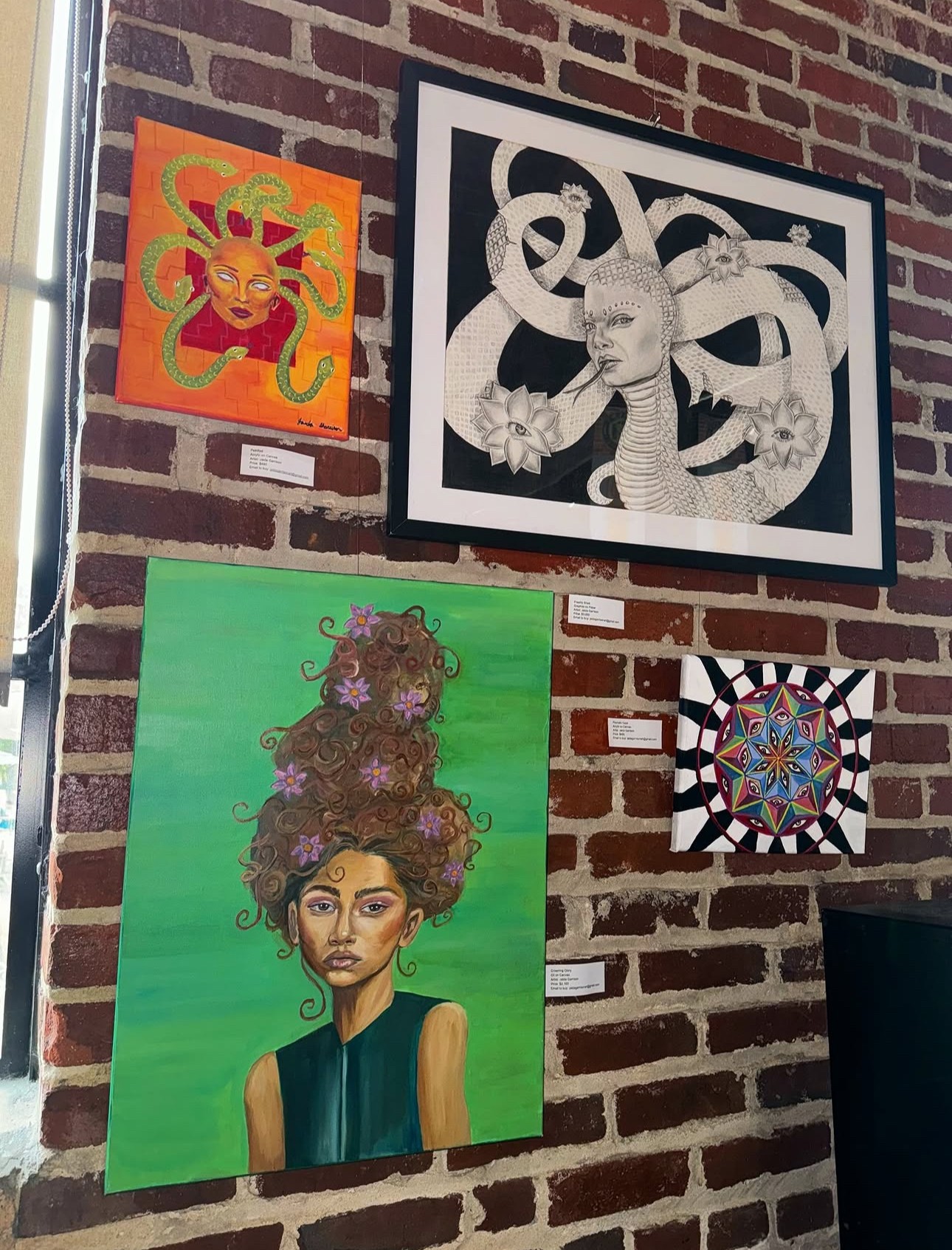 Brick wall with four colorful art pieces: a stylized orange and yellow face, a black and white octopus, a woman with a floral hairdo, and a geometric circular design.