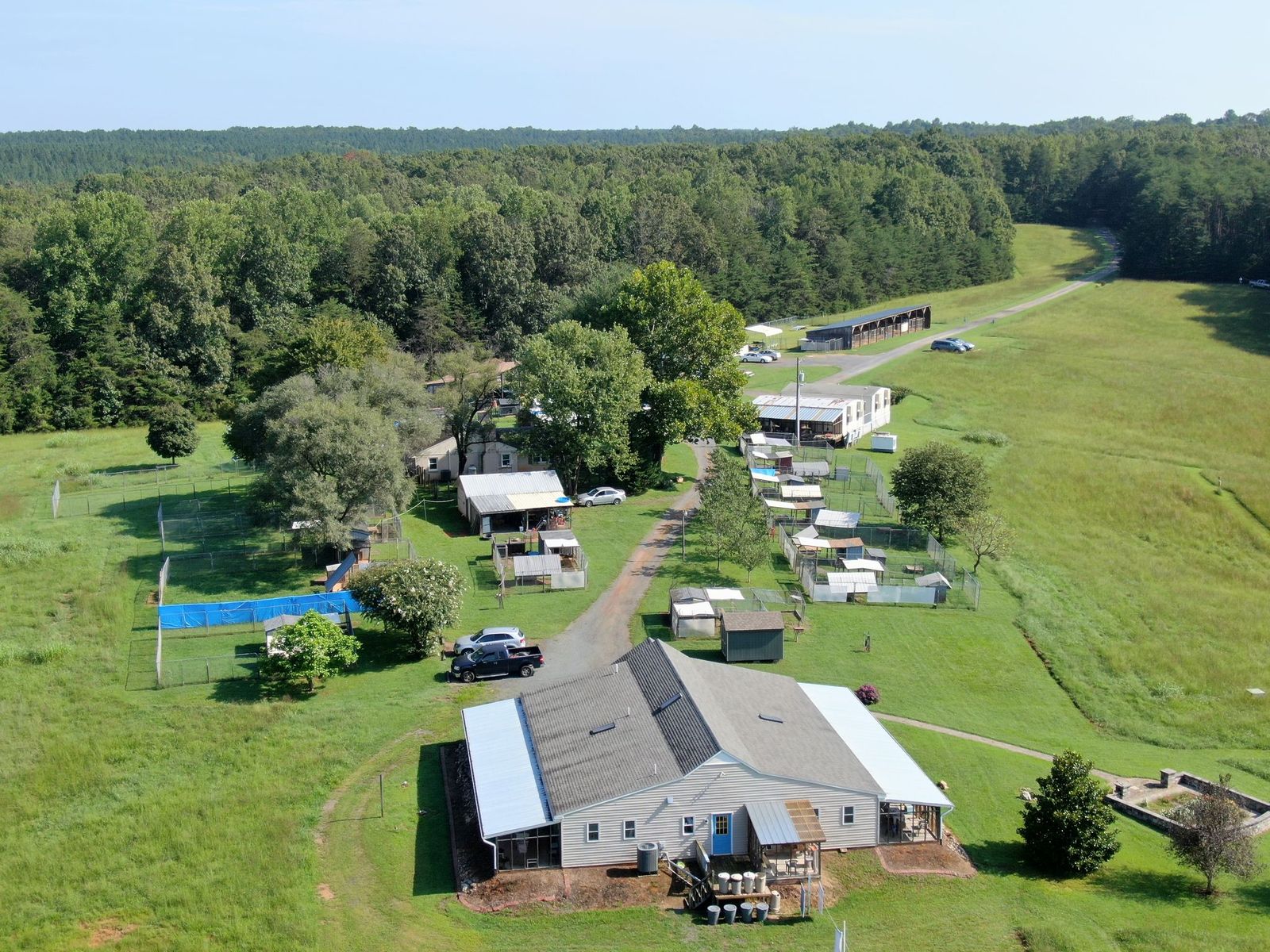 Aerial view of a campground with tents, trailers, and a building surrounded by trees and open grassy areas.