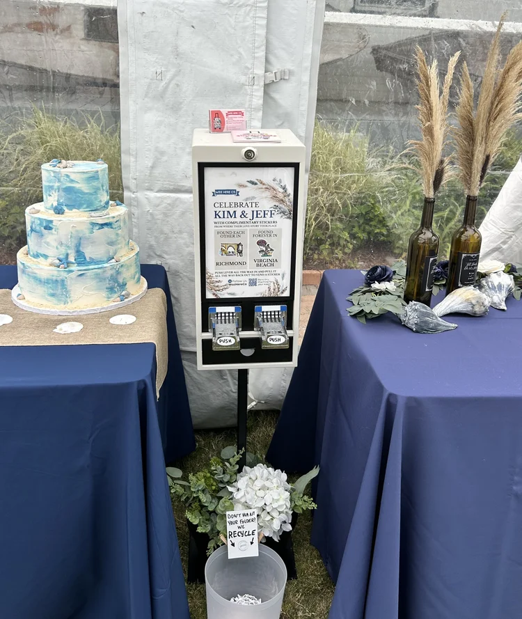 Display stand with event information, two tables with cakes and decorations, and plants in the background.