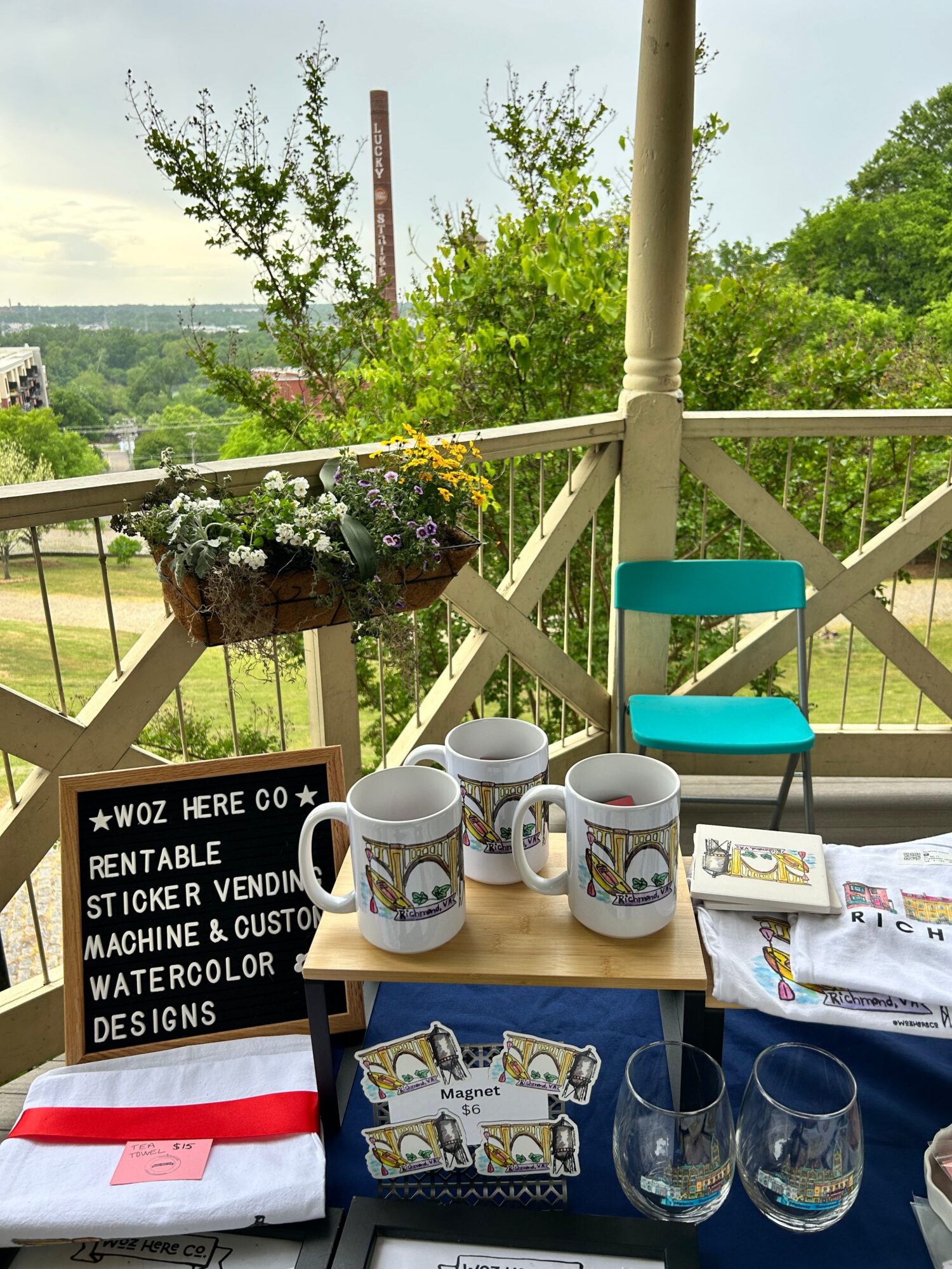 Outdoor table with cups, glasses, and decorative items, set on a balcony with a view of trees and water.