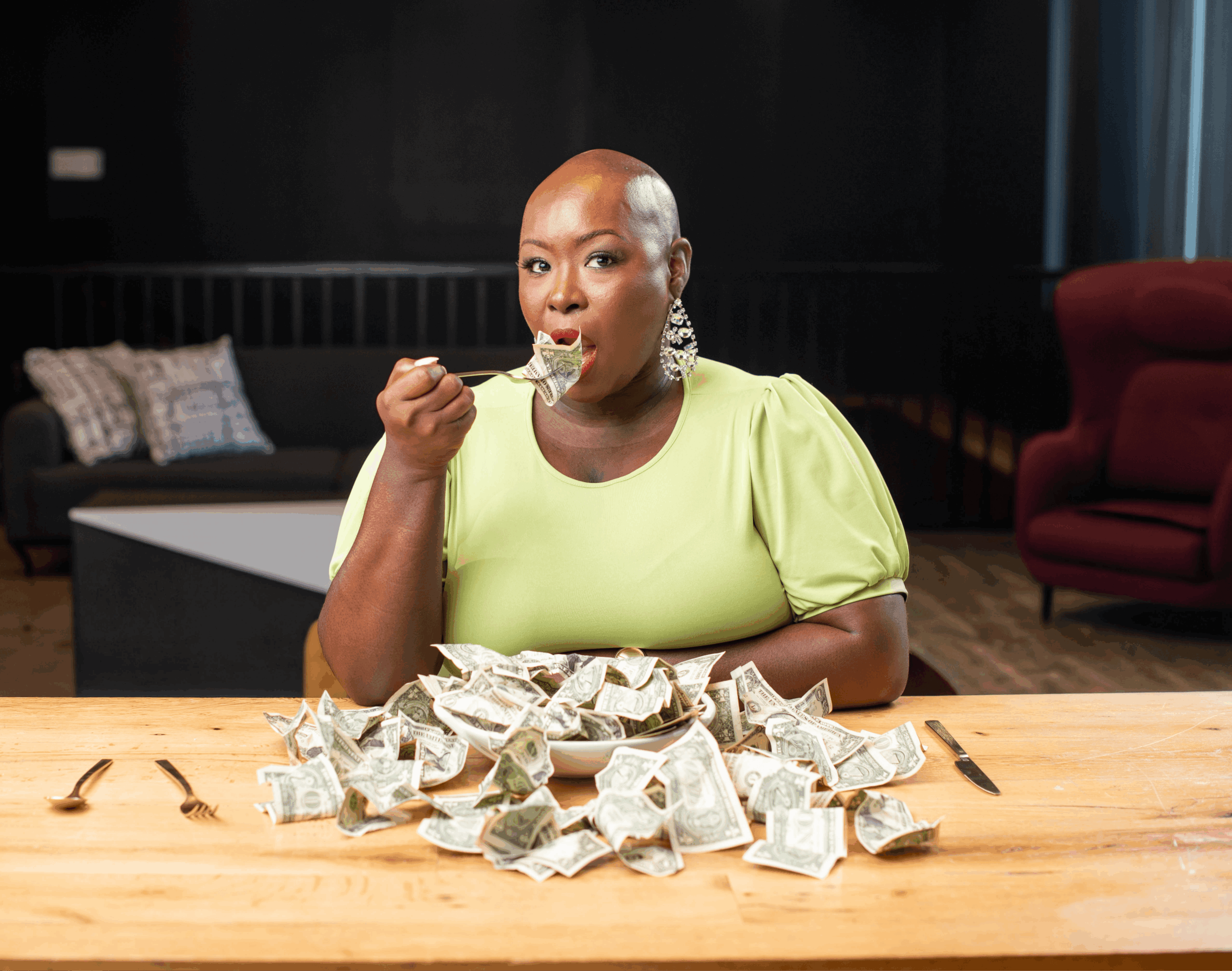 Woman with a shaved head eating with a fork, surrounded by crumpled paper on a wooden table.