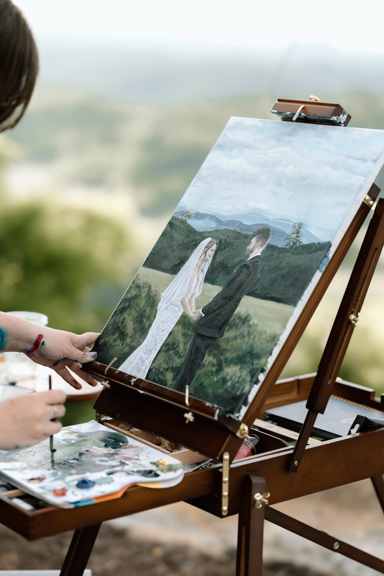 Person painting a landscape with a couple in the foreground, outdoors with a scenic background.