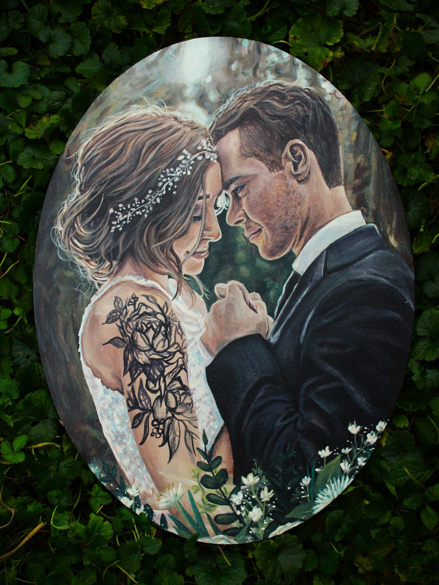 A couple in wedding attire face each other outdoors, holding hands, with greenery in the background.