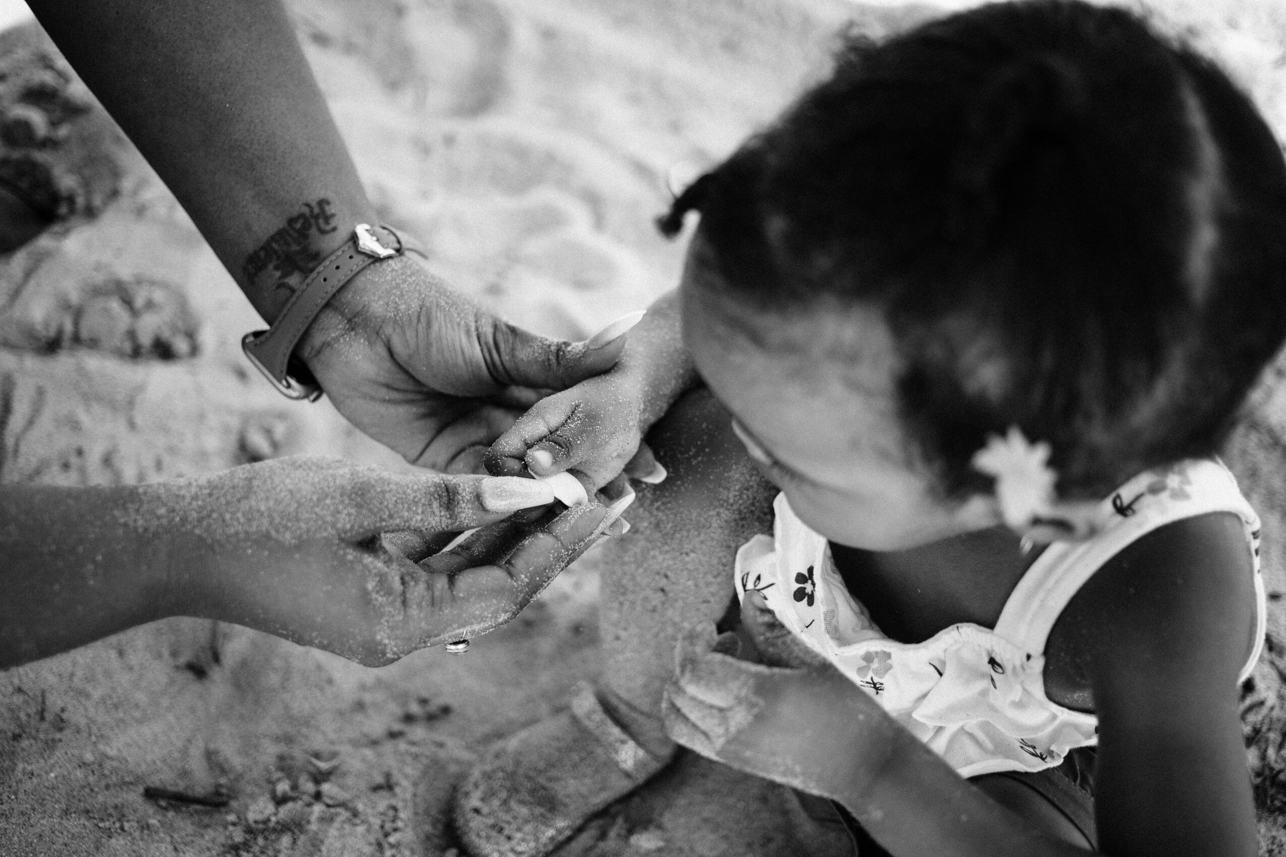 Child receiving a vaccination from a healthcare worker on a sandy surface, with the child's head turned downward.