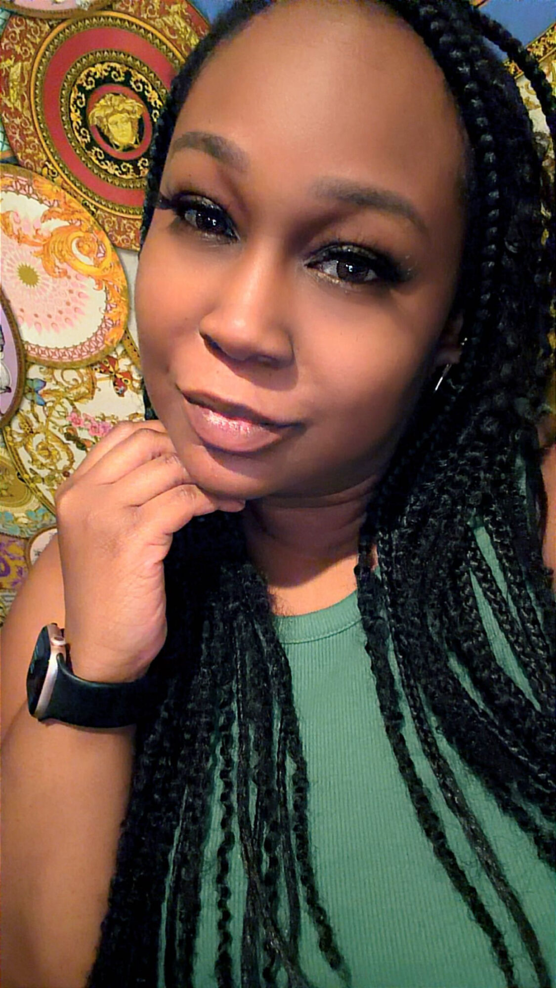 Close-up of a woman with braided hair, wearing a green top, posing with her hand near her face, colorful background