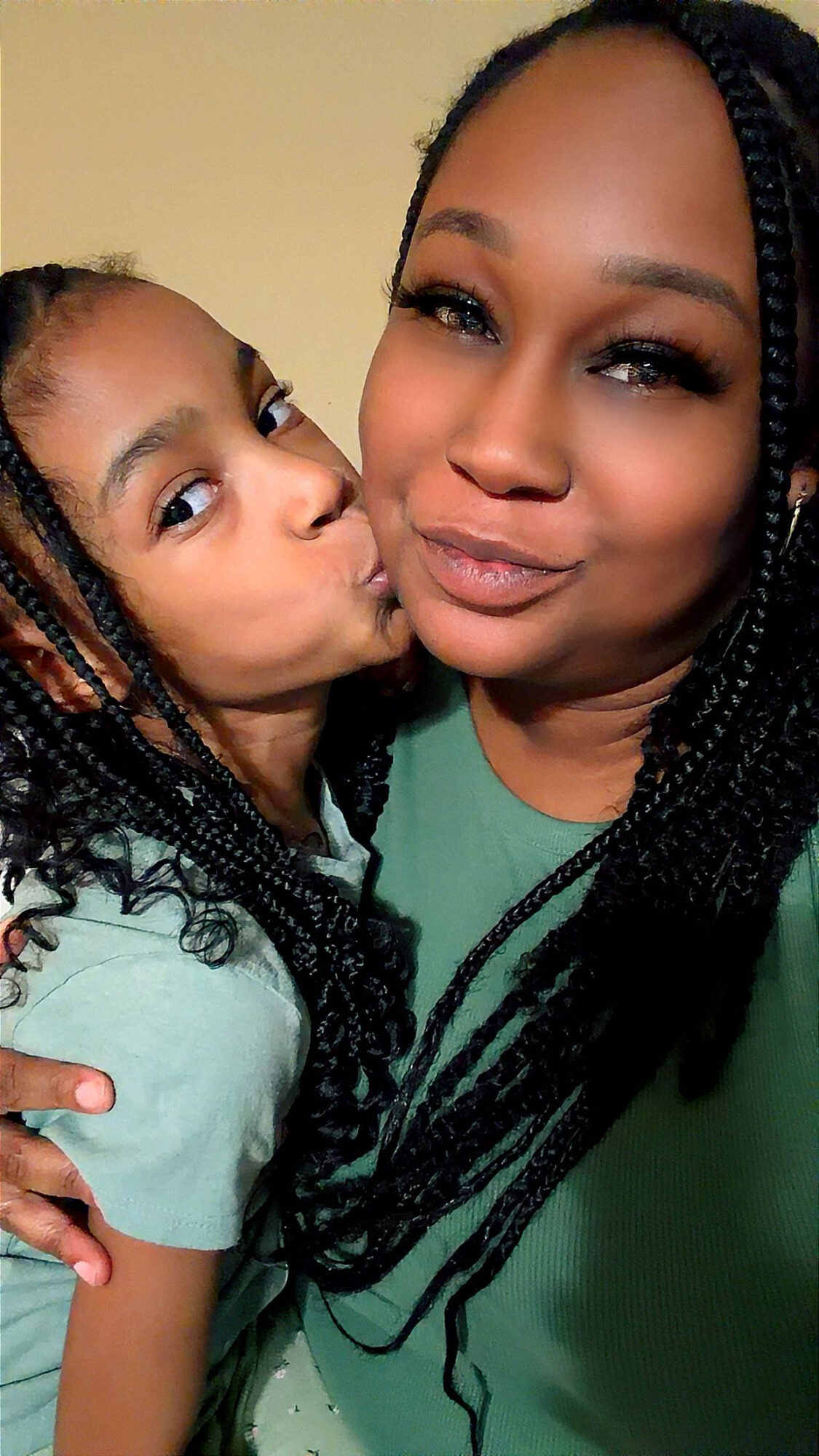 Two females close together, one with braided hair and the other with long braided hair, both smiling.