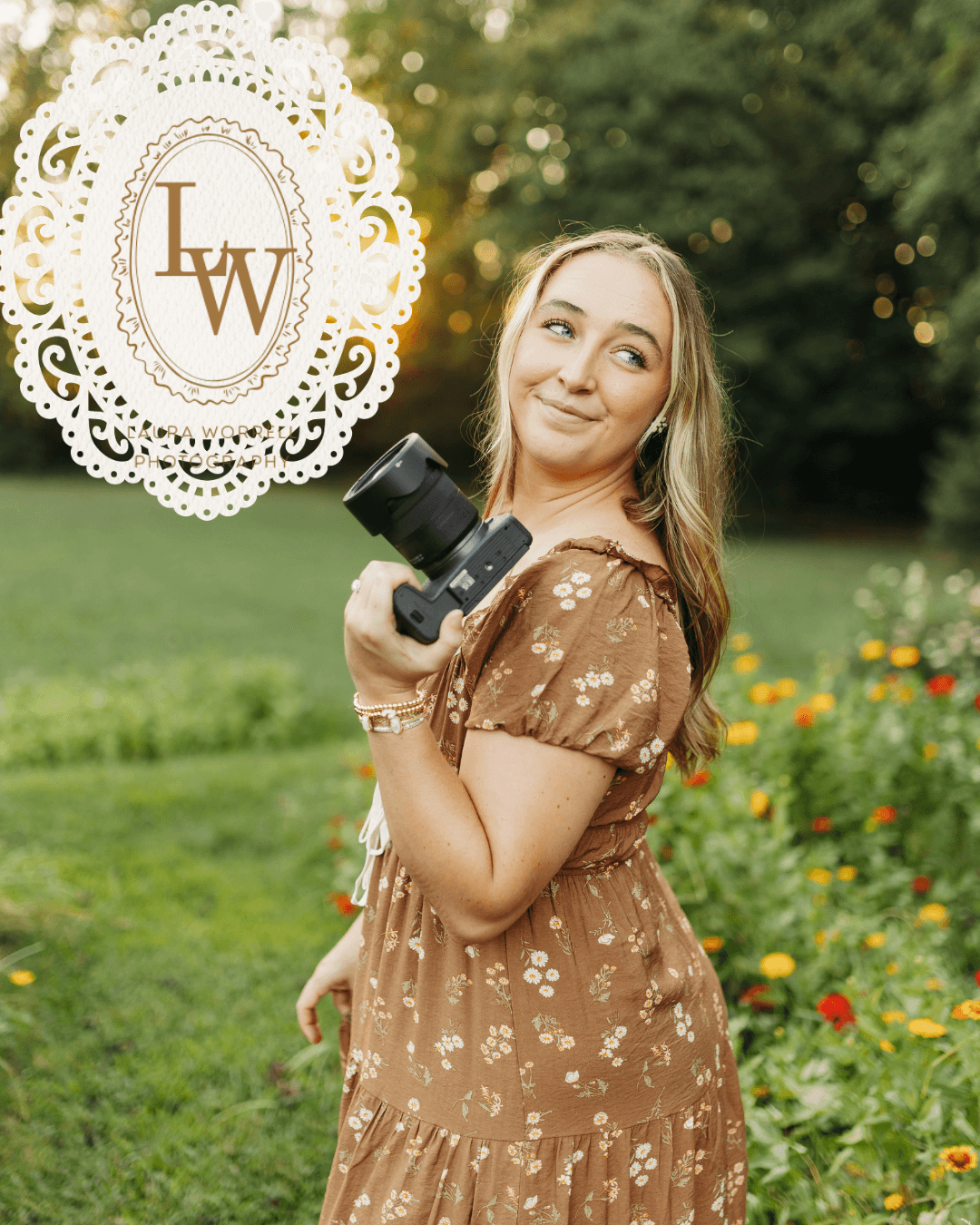 Young woman holding a camera outdoors in a garden with flowers and trees, smiling and looking to the side.
