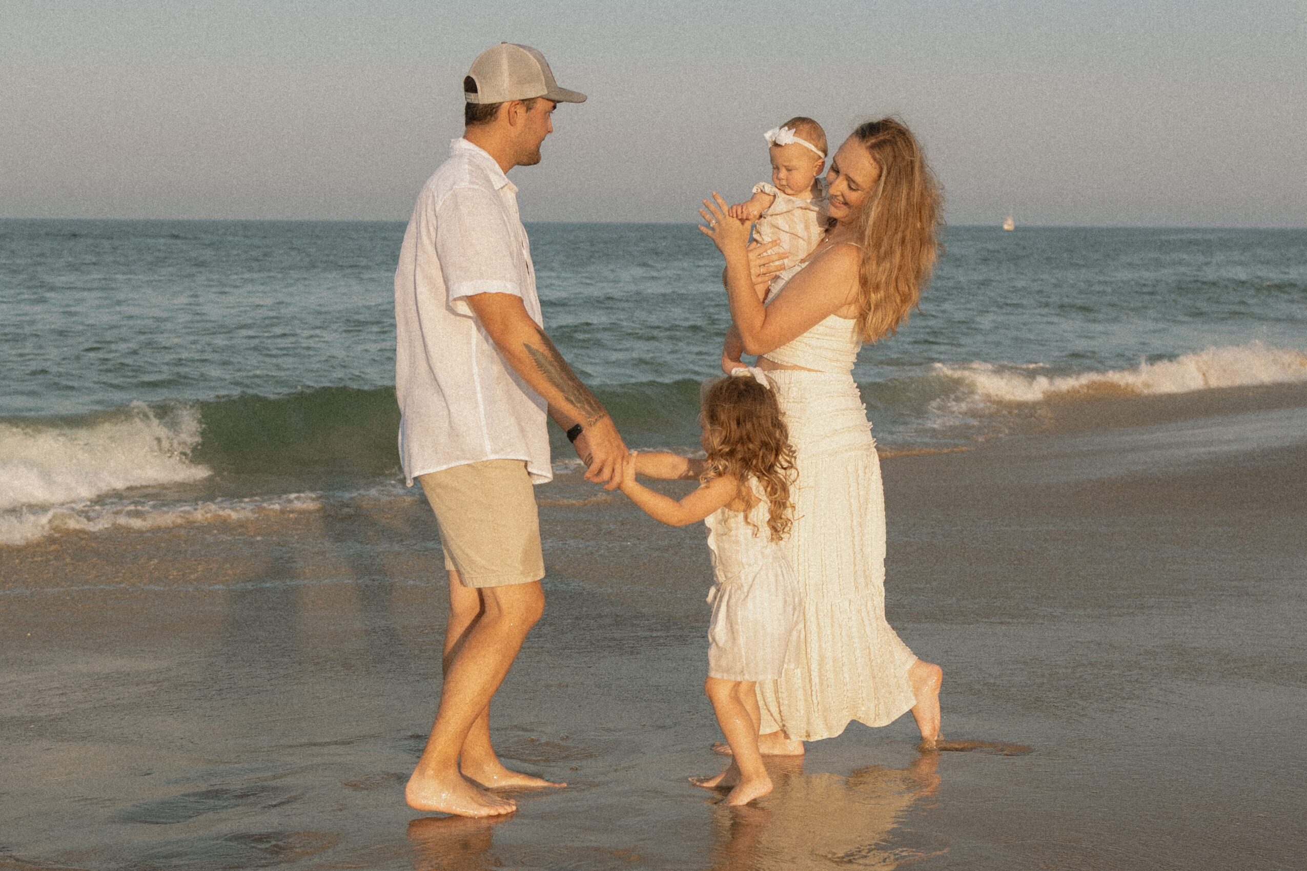 Family of four on the beach, holding hands, with ocean waves in the background, during daytime.