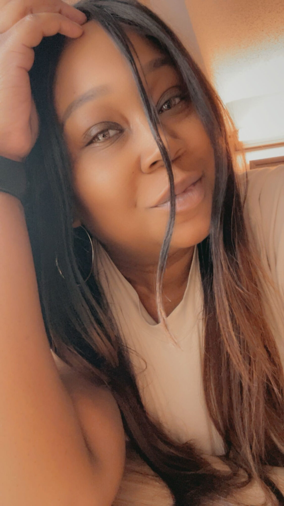 Close-up of a woman smiling, resting her head on her hand, with long hair and a light-colored top.
