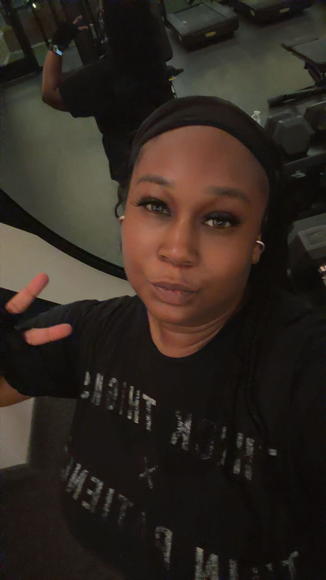 Woman with headband taking selfie, background shows cars and a person in a parking garage.