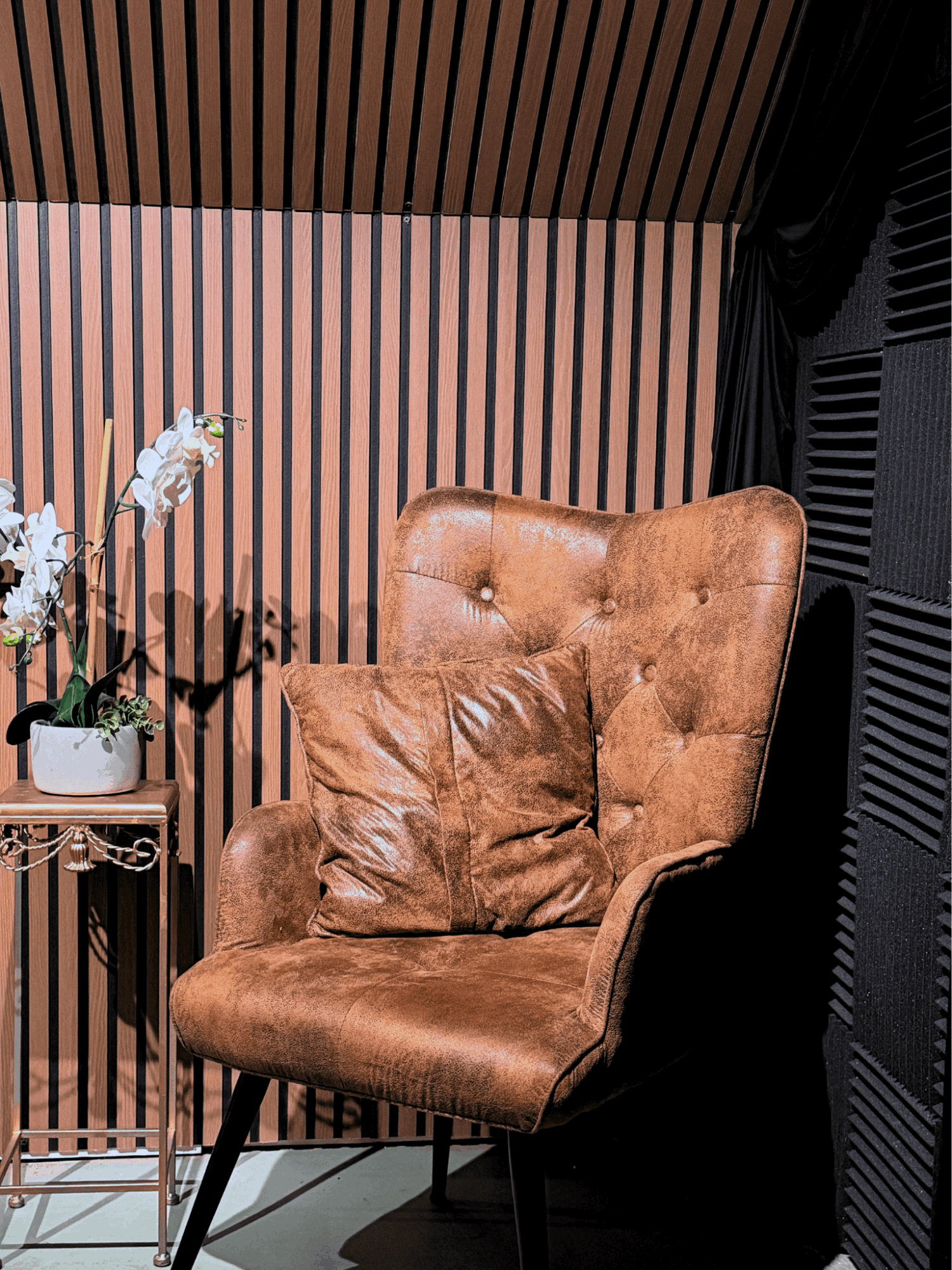 Brown leather armchair with a matching pillow, set against a striped wall with a small table holding a plant nearby.