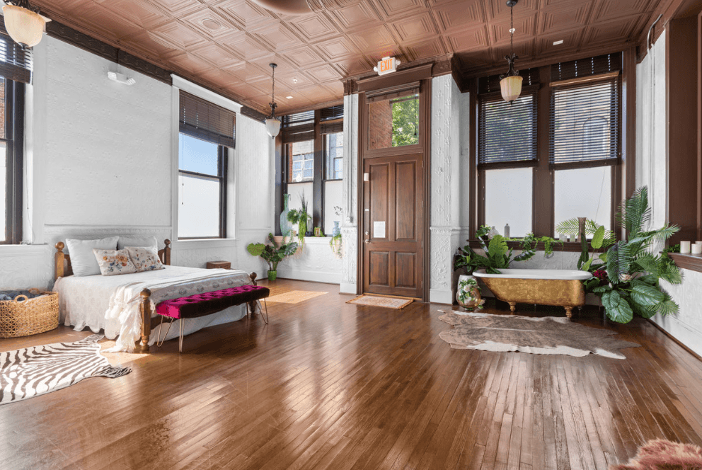 Spacious living room with wooden floors, large windows, a white sofa, plants, and a wooden door, bright and airy.
