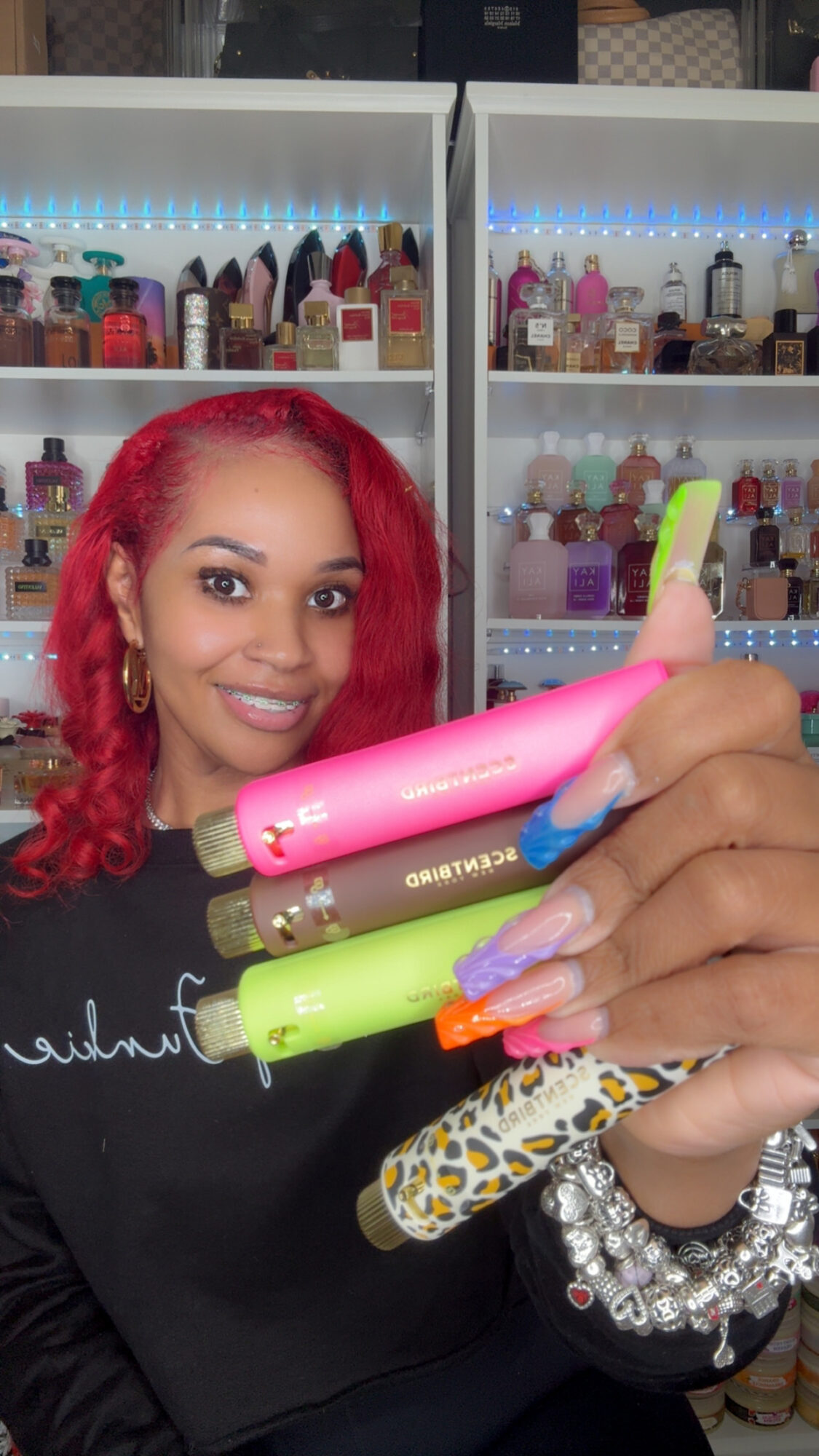 Person with red hair holding colorful curling irons in front of shelves with beauty products.