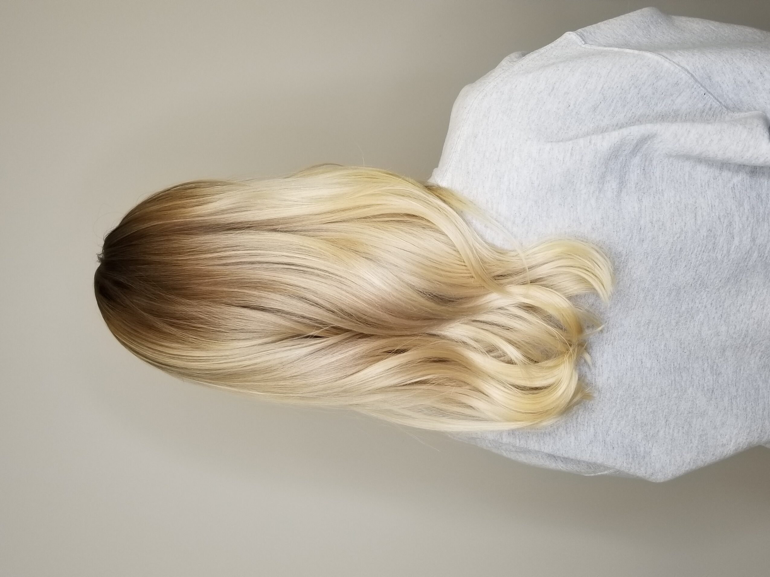 Person with long, wavy blonde hair wearing a gray shirt, facing away from the camera.