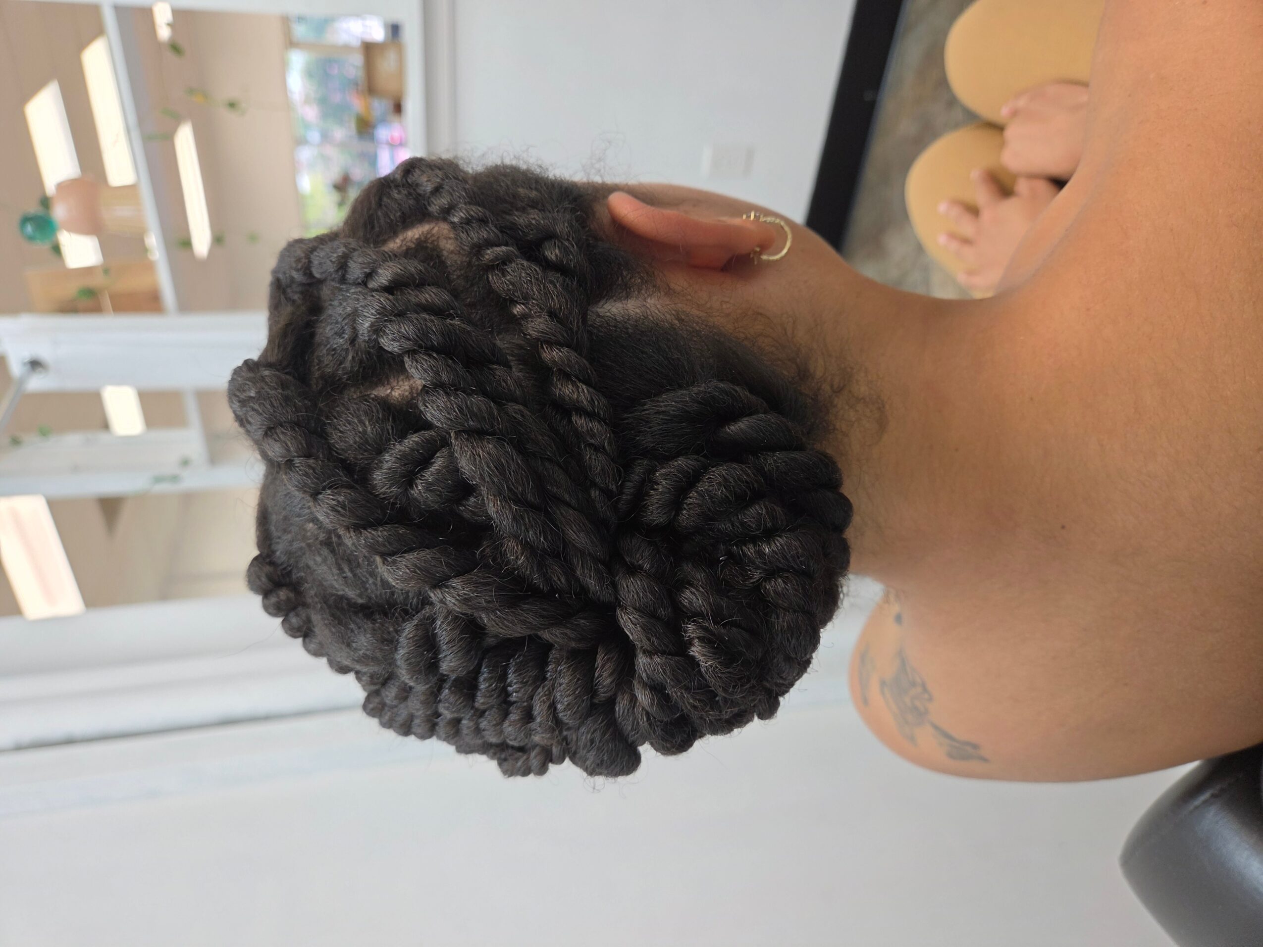 Side view of a person with braided hair styled into a bun, showing the back of their head and neck.