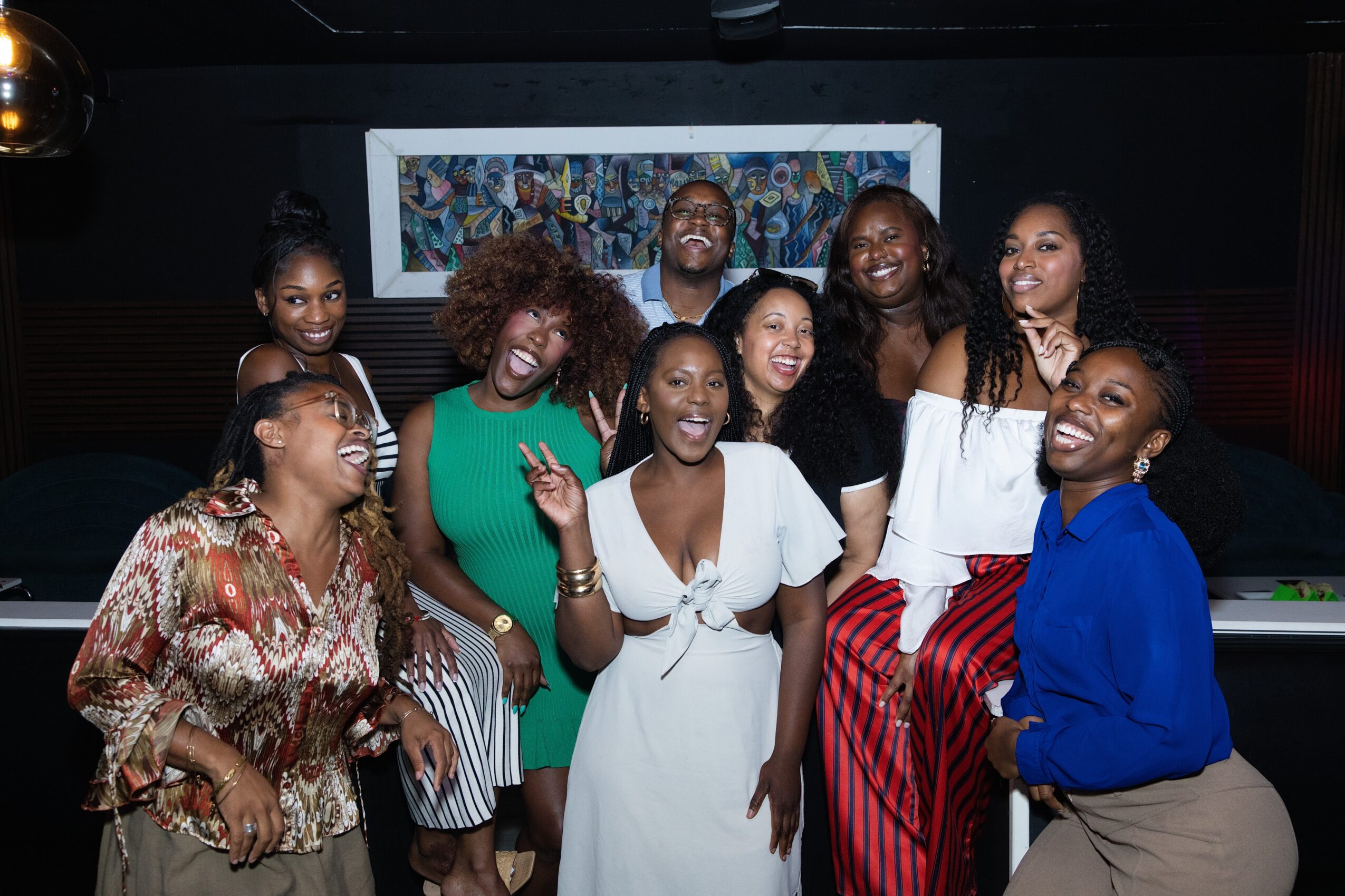 Group of eight women smiling and posing together in a photo booth, with a colorful background screen behind them.