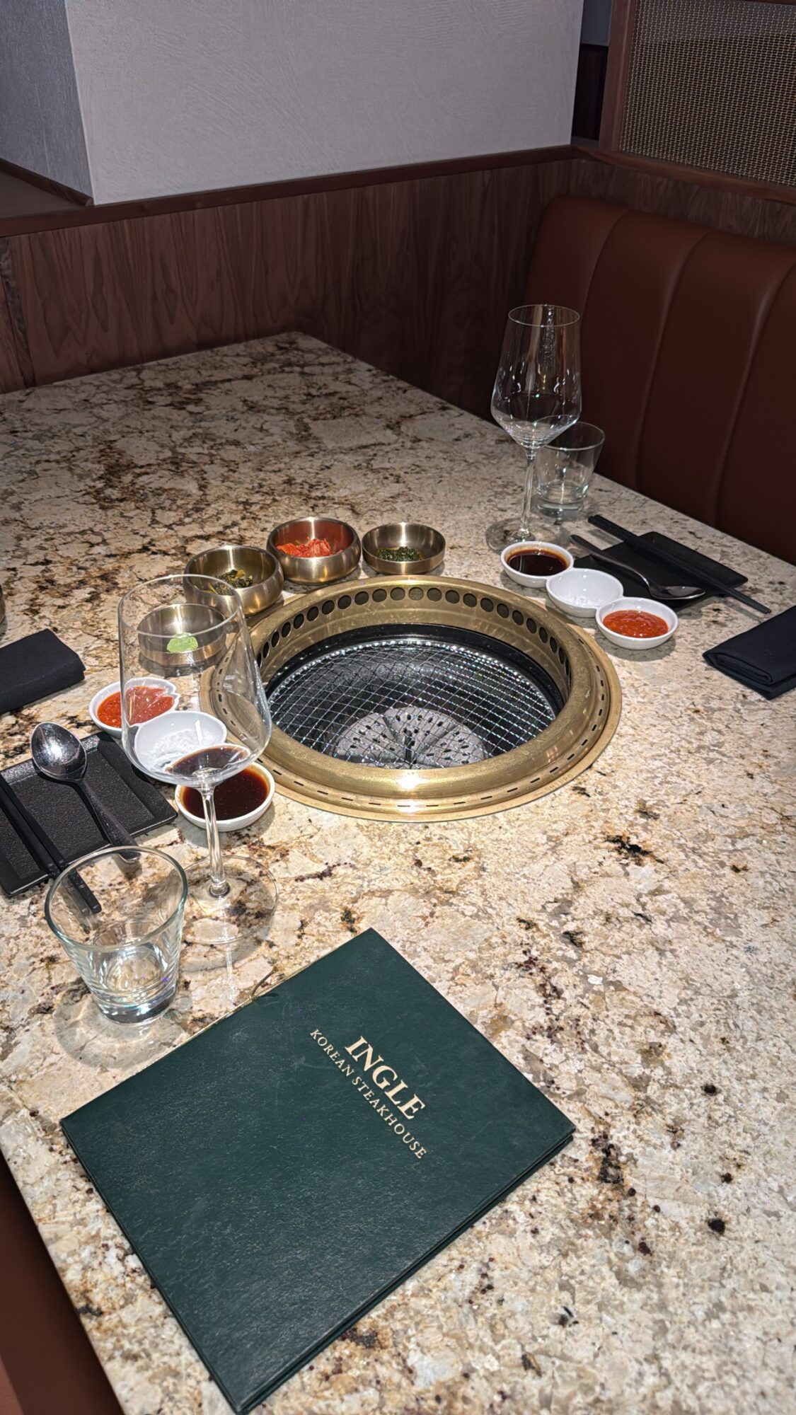 Restaurant table with built-in grill, glasses, sauces, and a menu, set for dining.