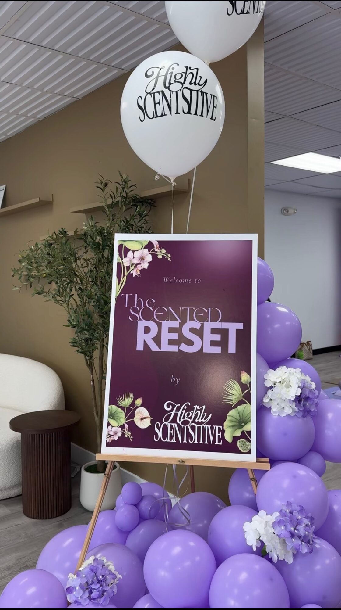 Sign with purple background and white flowers, reading 'The Secret to Reset' and 'High Sensitive,' surrounded by purple balloons.