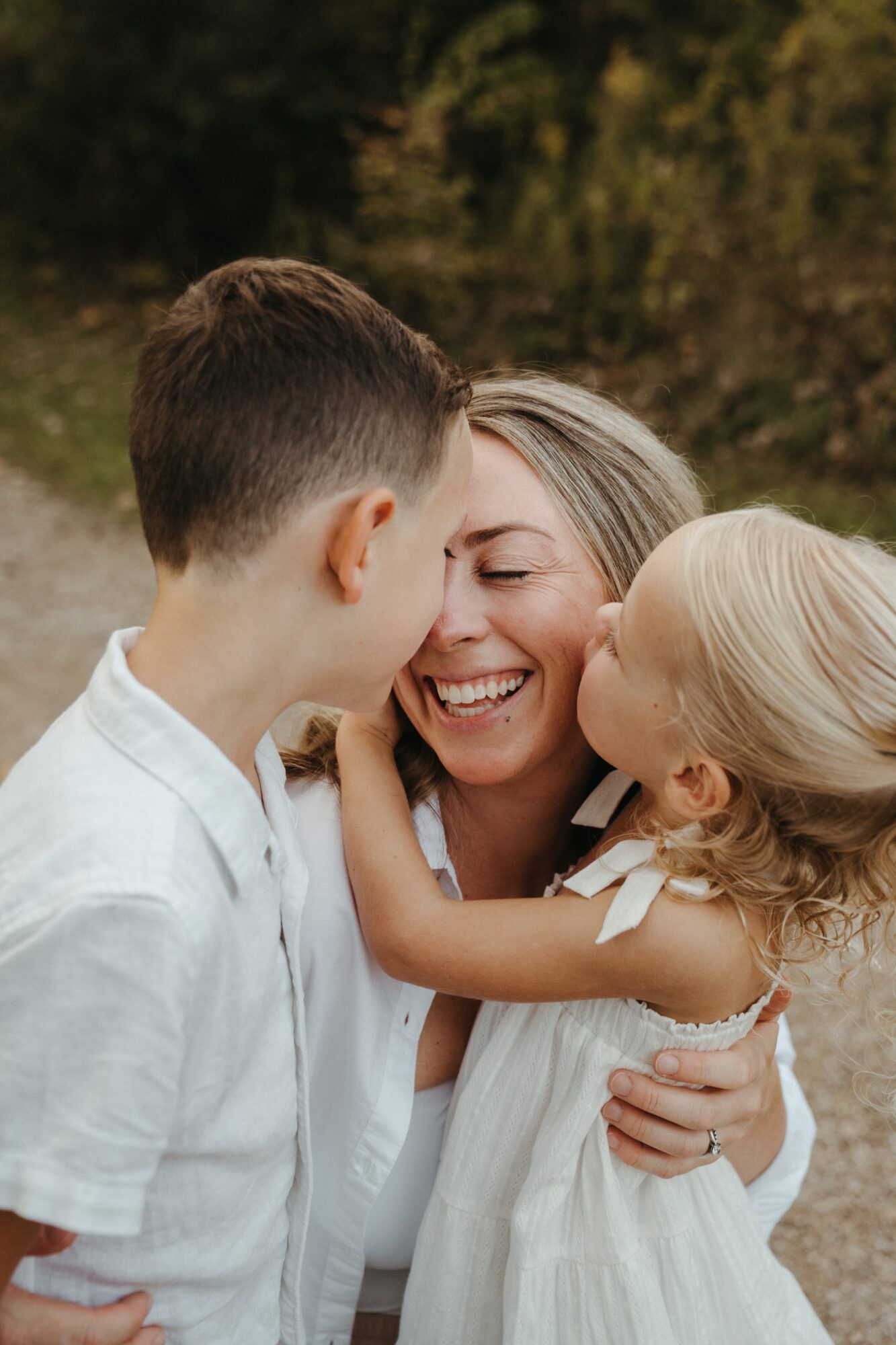 Woman smiling with two children outdoors, one girl and one boy, close together, joyful moment, natural background