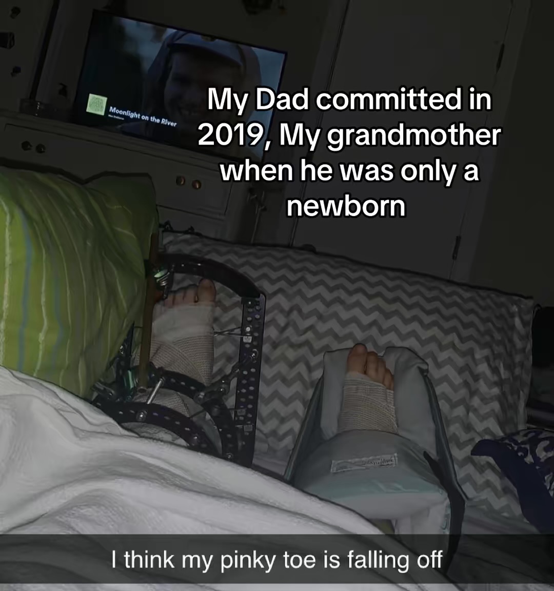Person's foot with a pinky toe visible, lying on a bed with a blanket and pillow, in a room with a TV. Word count: 20