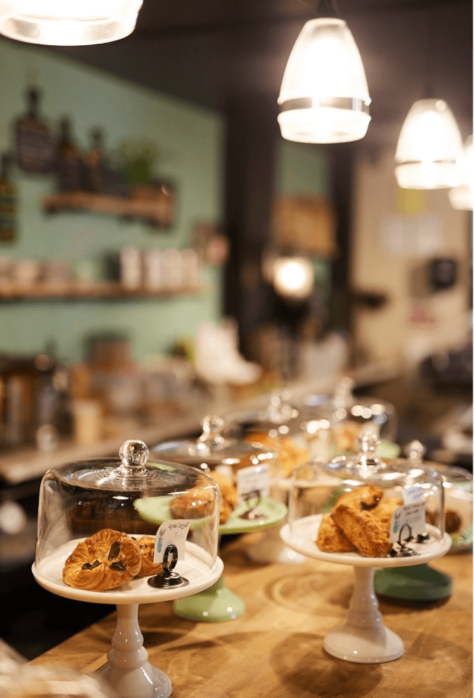 Desserts on white cake stands in a cozy cafe with hanging lights and blurred background.