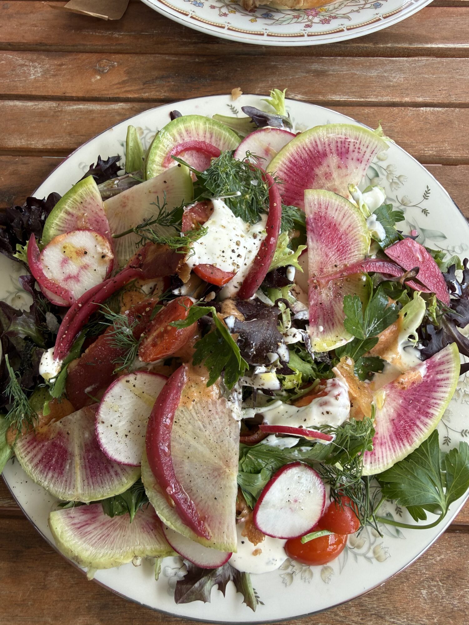 Fresh salad with sliced radishes, greens, and vegetables on a white plate, on a wooden table.