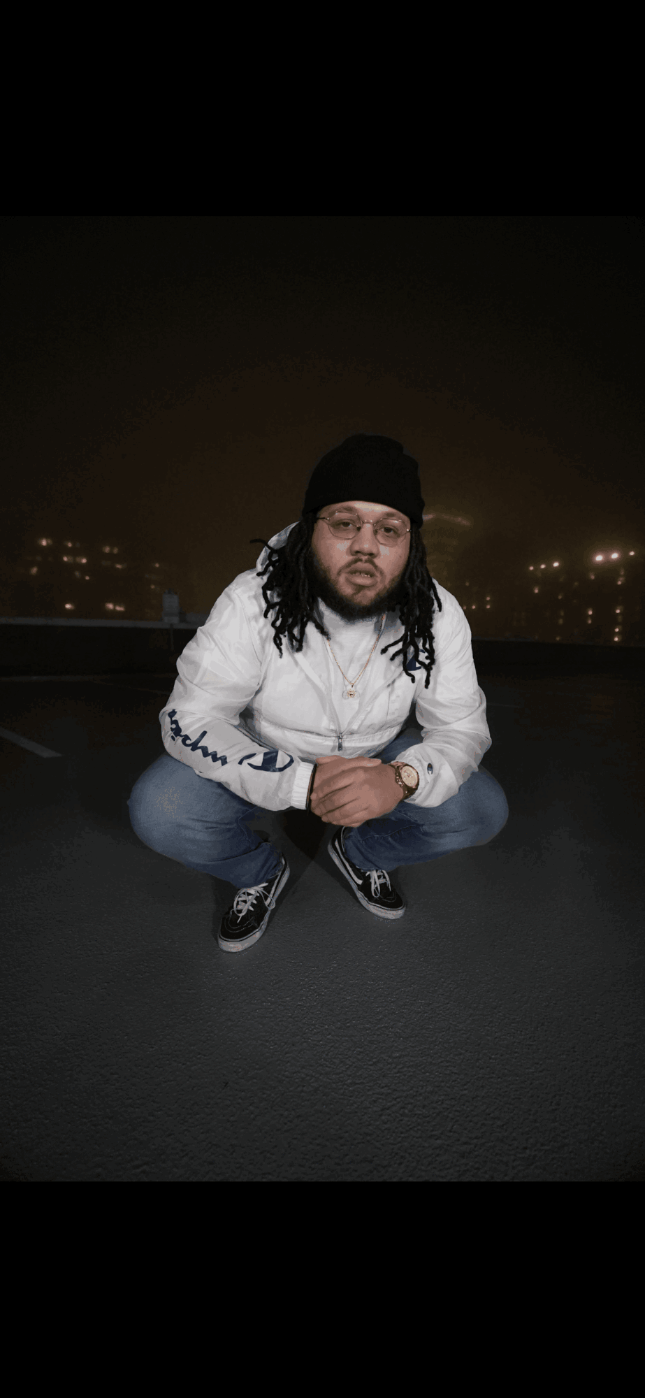 Person crouching on a dark pavement at night, wearing a black beanie and a white jacket.