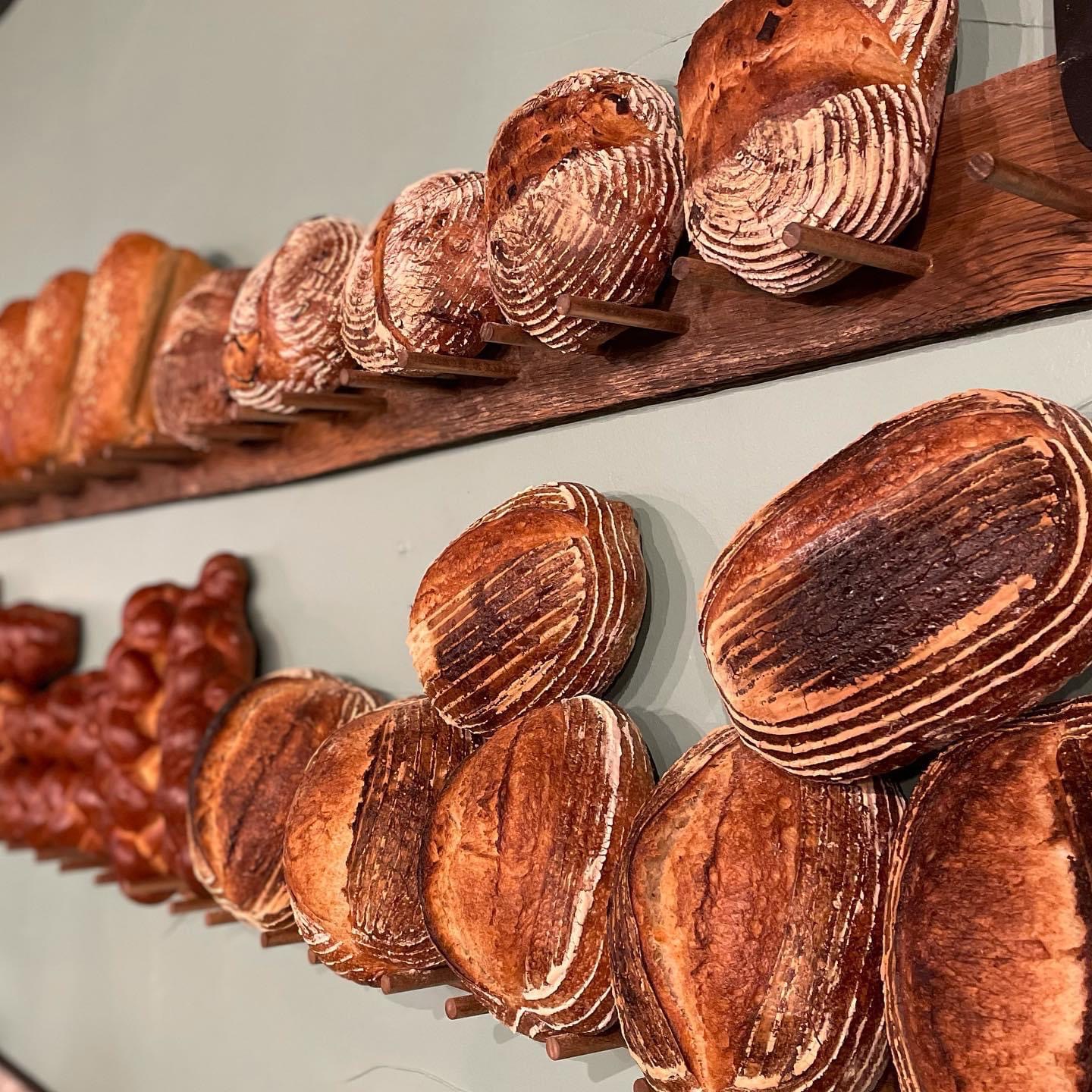 Close-up of wooden shelves with various bread loaves, including striped and round shapes, displayed in a bakery setting.