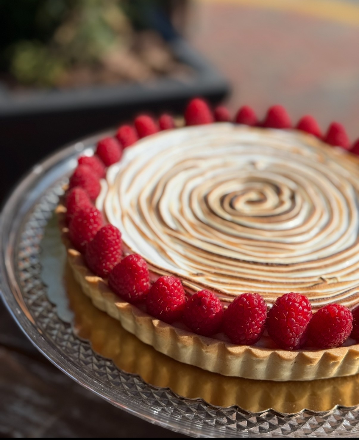 Round dessert with a raspberry border and a swirled topping on a silver tray.