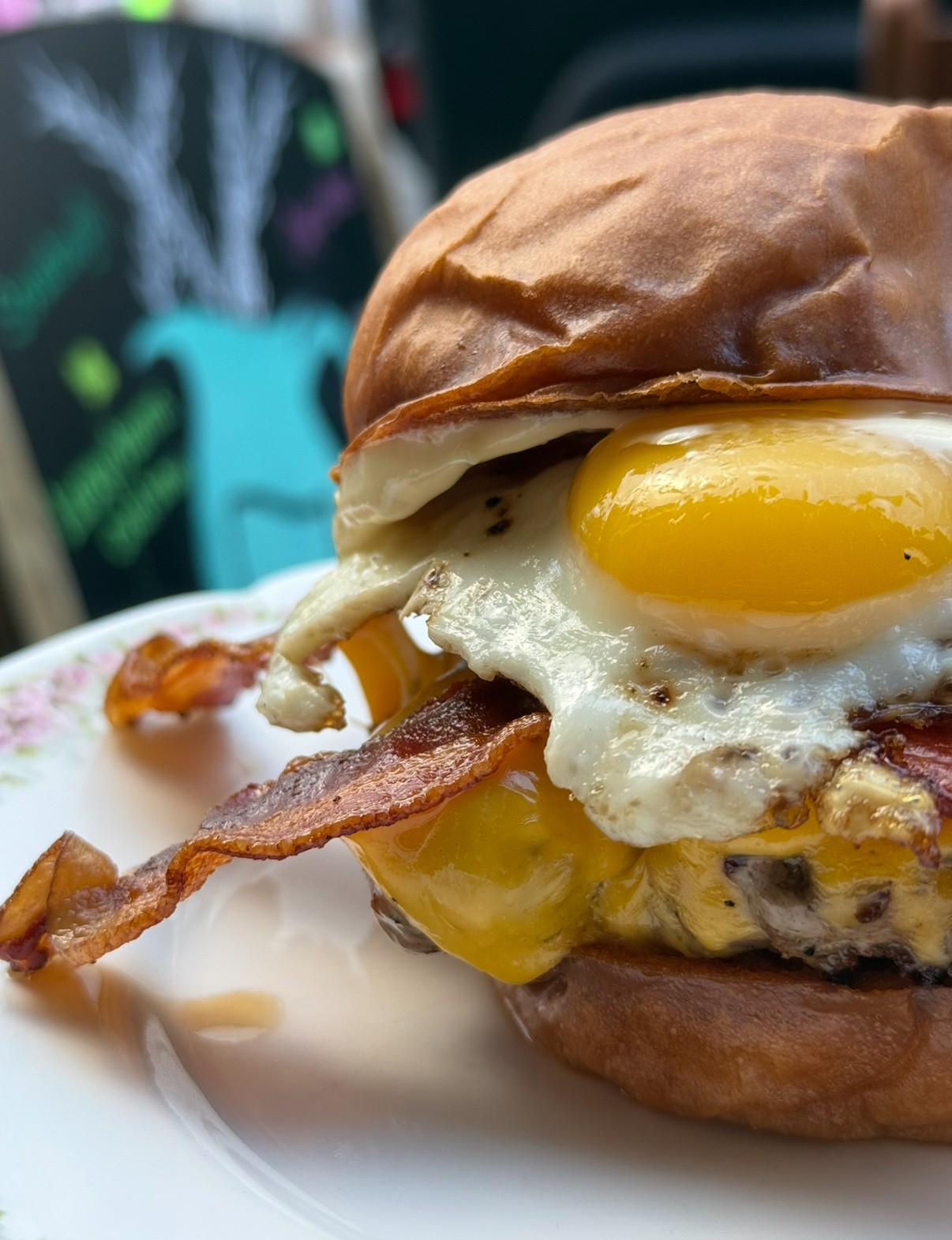 Close-up of a burger with a fried egg, bacon, and cheese in a bun on a plate.