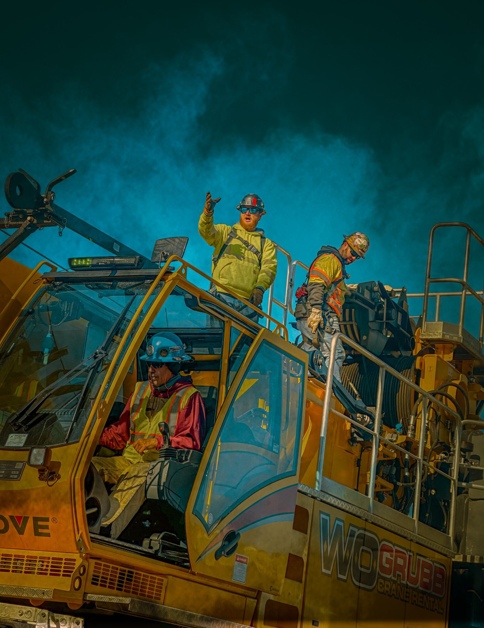 Three rescue workers in yellow uniforms and helmets on a yellow rescue vehicle, one waving, others preparing equipment, smoke in background.