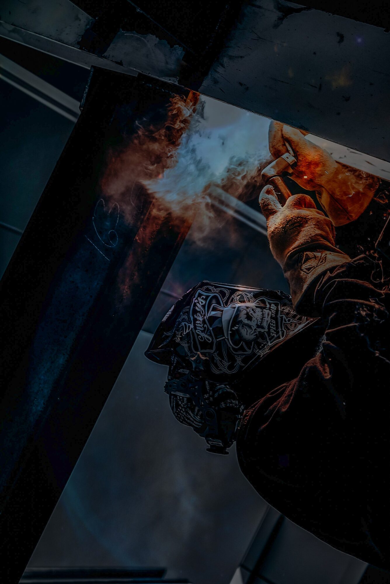 Person holding a lit cigarette with smoke and flames, wearing a patterned jacket, in a dark setting.