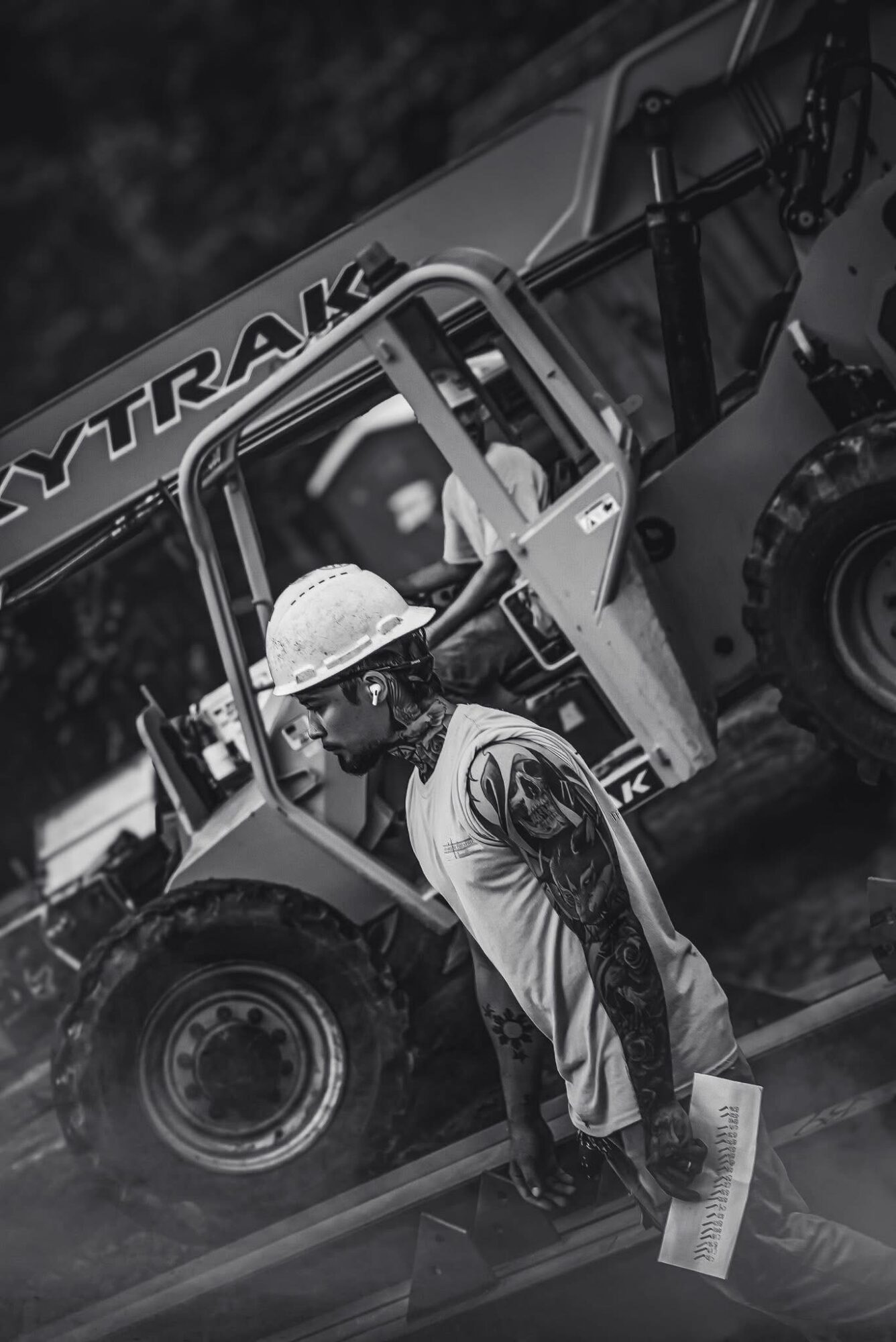 Person with tattoos and a hat walking past a construction vehicle with a sign reading 'TRAK'.