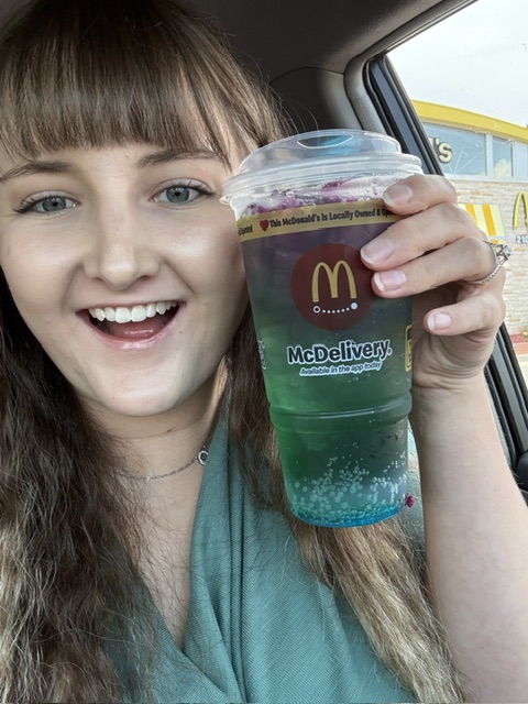 Young woman with long hair smiling and holding a McDelivery drink inside a car.