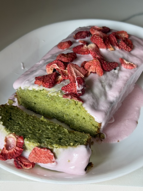 Two slices of green cake with pink icing and strawberry toppings on a white plate.