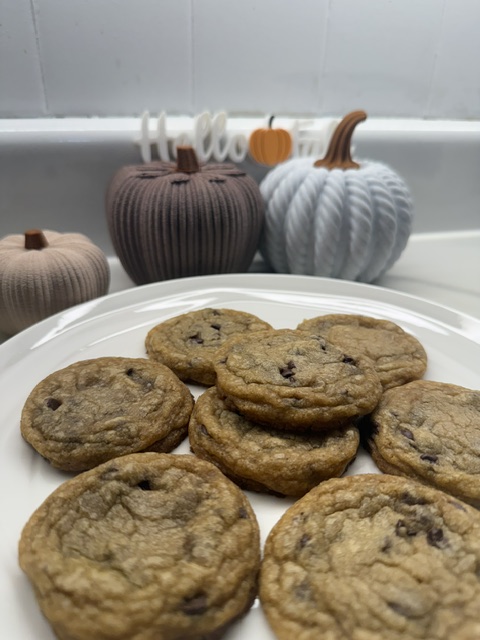Plate of chocolate chip cookies with a kitchen background, including decorative pumpkins, in a neutral setting.