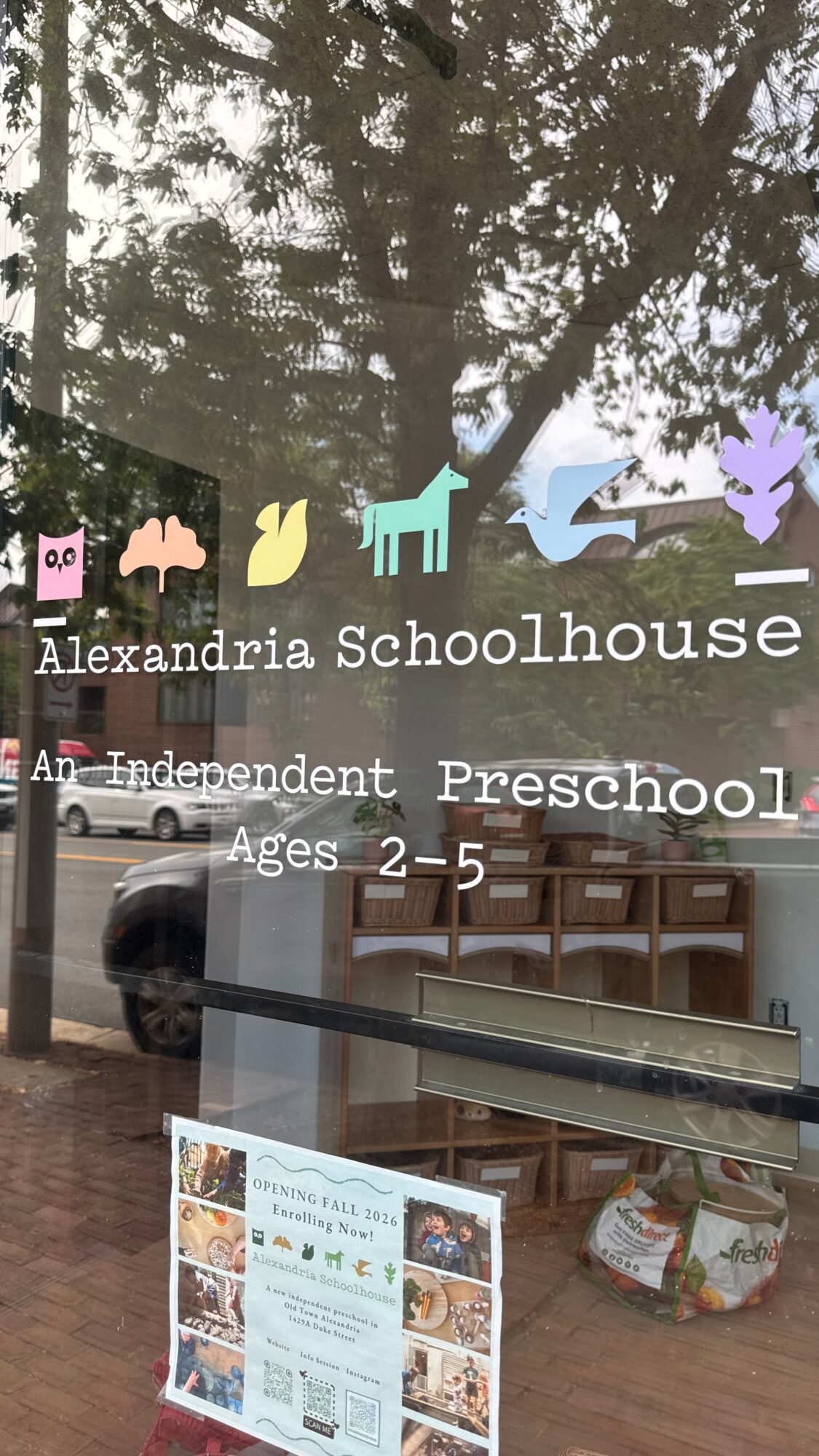Schoolhouse window with colorful animal and tree stickers, text about Alexandria Schoolhouse Preschool, and a display of posters inside.