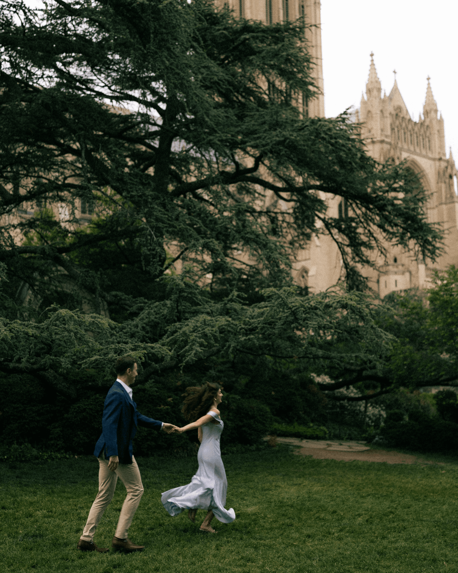 A couple dancing outdoors near a large tree with a historic building in the background.