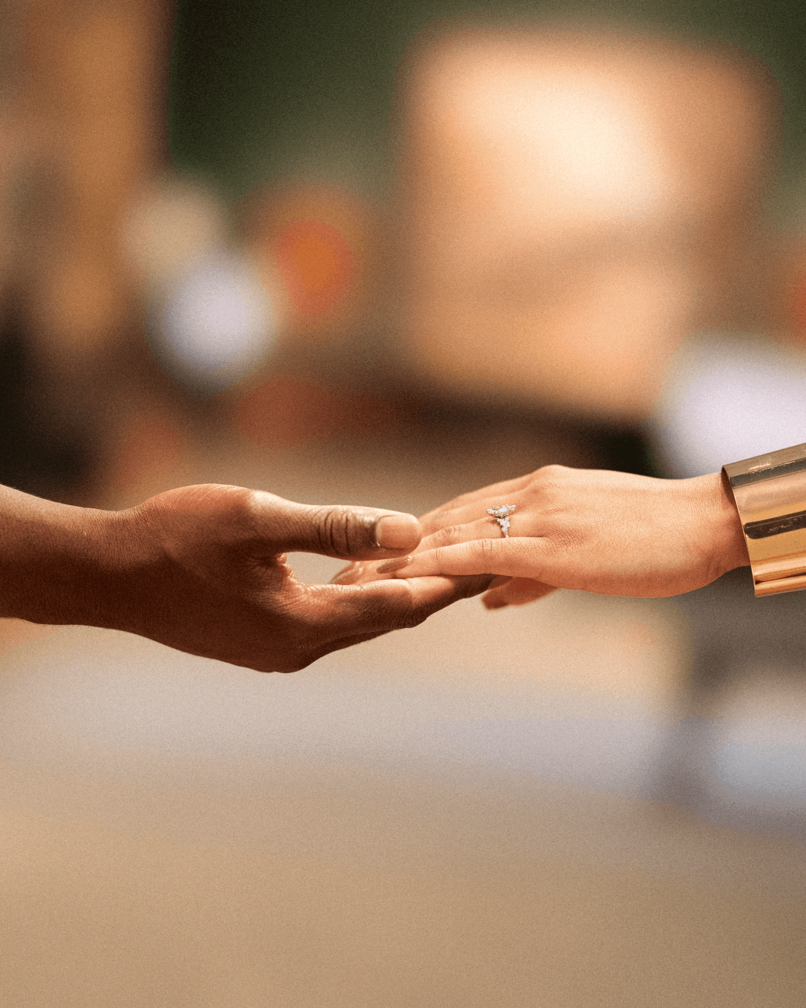 Two hands gently touching, one with a ring, in a blurred background.