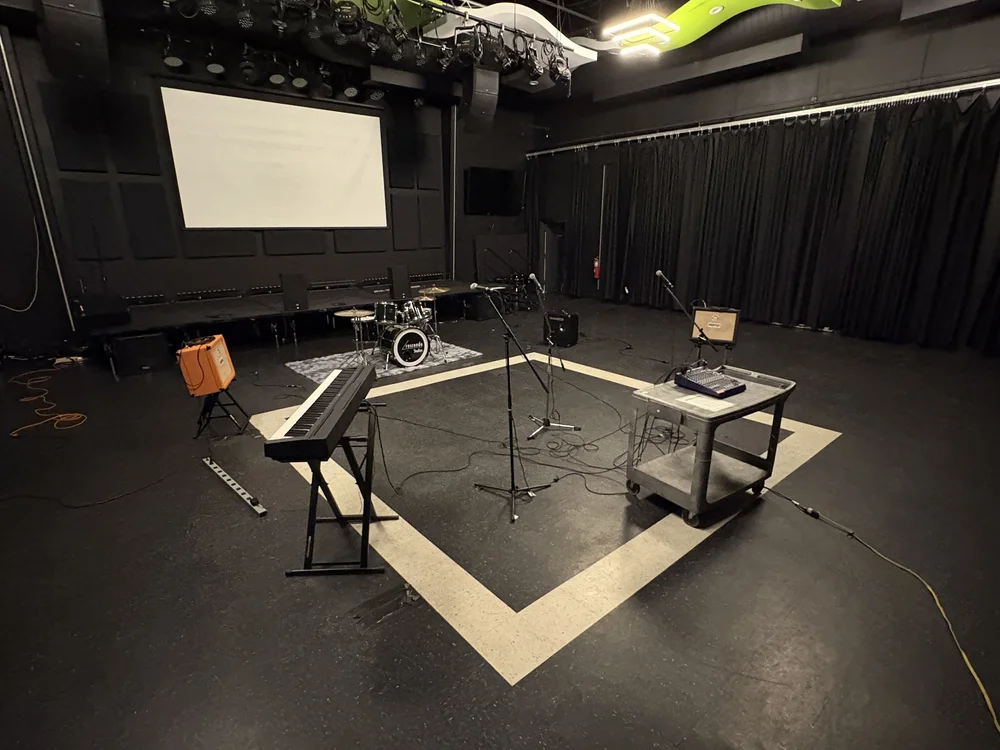 Empty stage with musical instruments, microphone, and equipment, black curtains, and a large screen in the background.