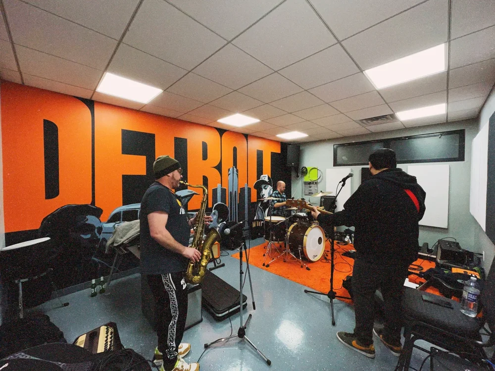 Musicians practice in a room with orange and black decor, including a large