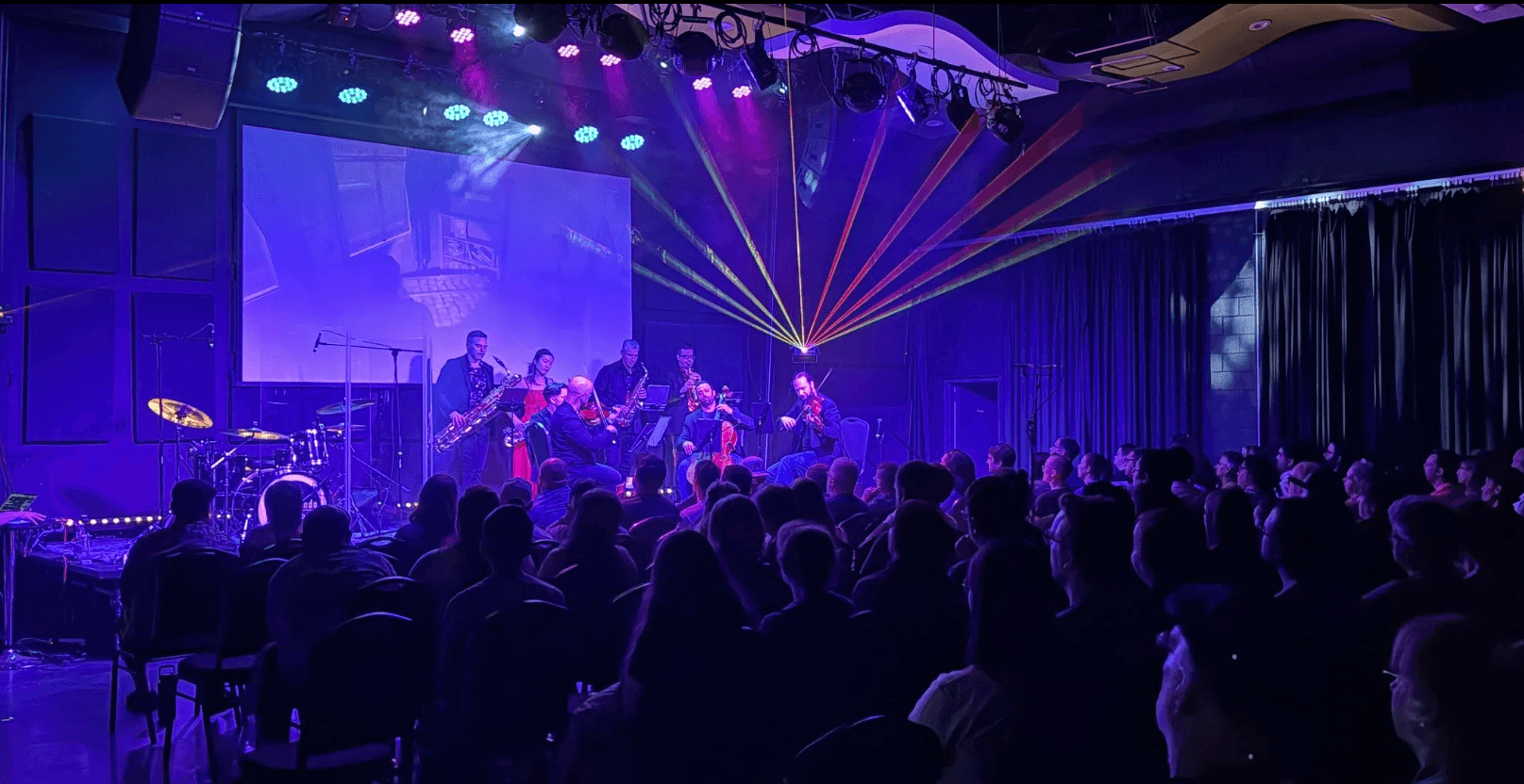 Concert stage with performers, colorful laser lights, and an audience watching attentively.
