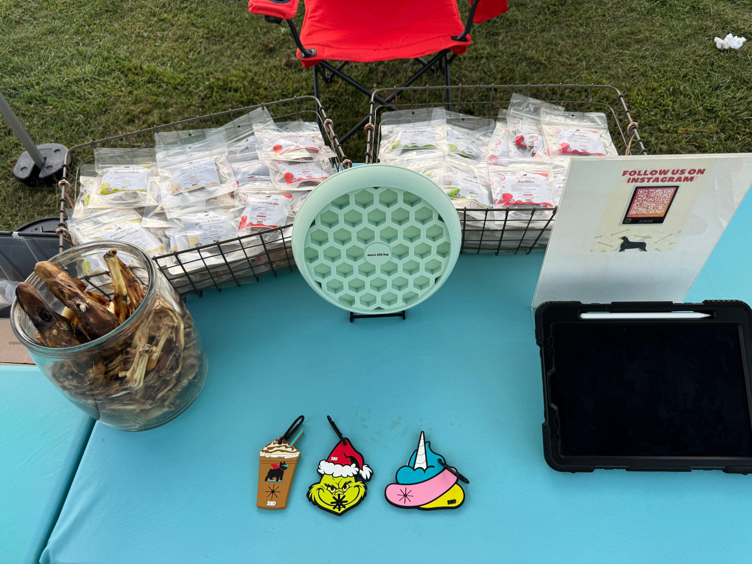 Table with candy, a container of wrapped chocolates, a green circular item, and a display with a screen, outdoors.