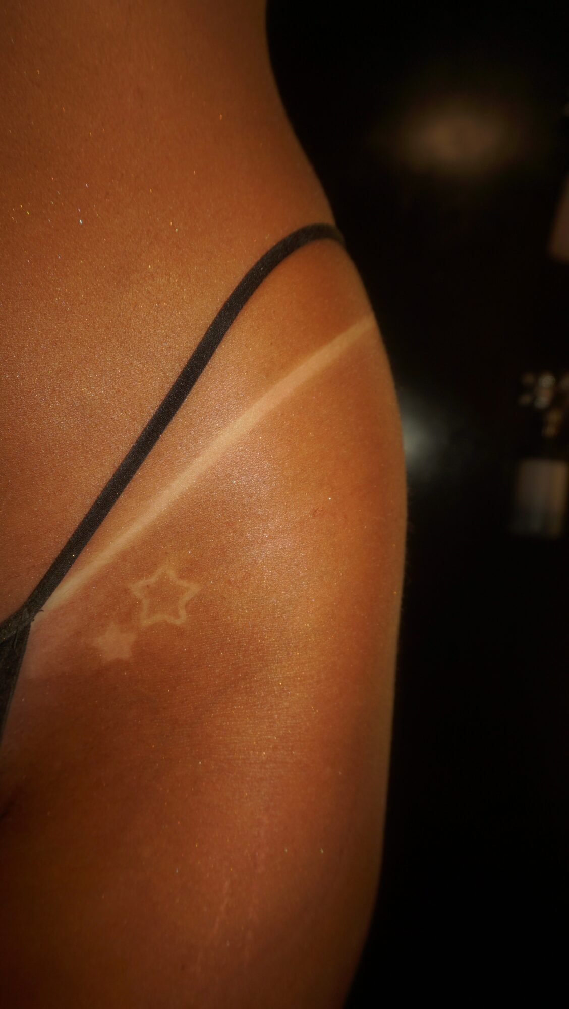 Close-up of a person's shoulder with a star-shaped tattoo and a light-colored line, dark background.